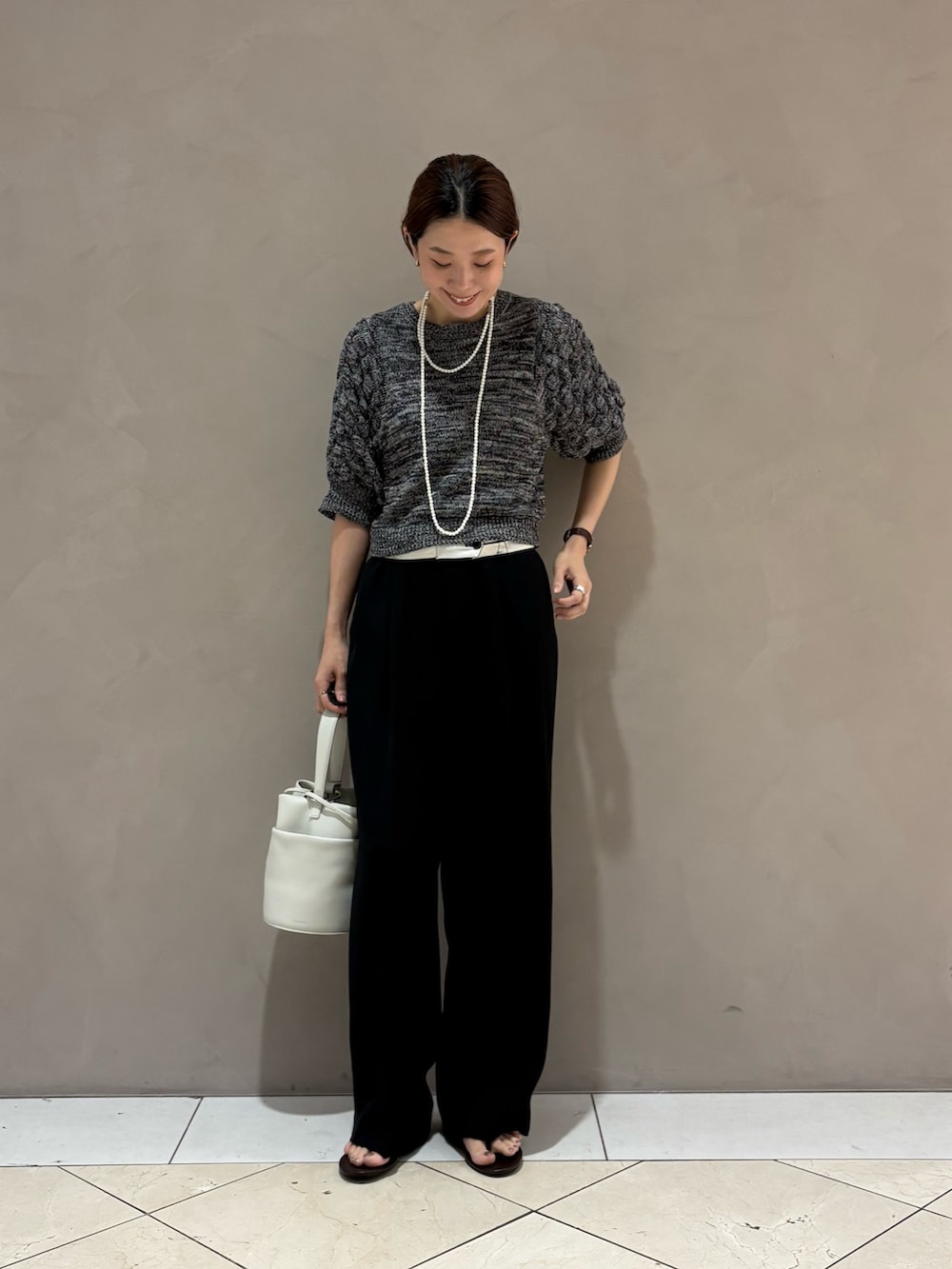 グレー系のニット/セーター、ブラック系のその他パンツ、ホワイト系のハンドバッグを着用したレディースの夏コーディネートの5枚目の写真