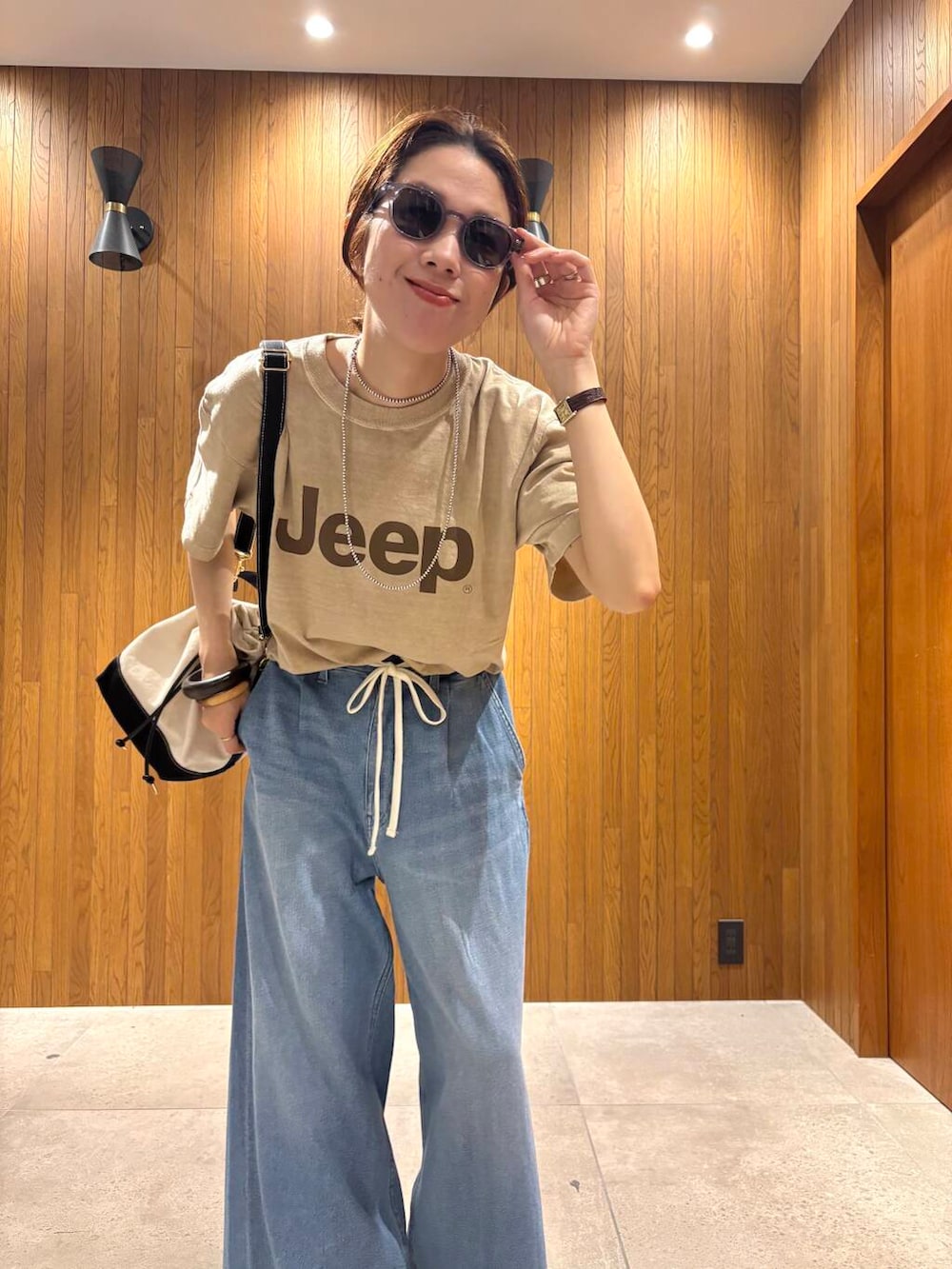 ブルー系のデニムパンツ、ブラック系のサンダル、ベージュ系のTシャツ/カットソーを着用したレディースの夏コーディネートの6枚目の写真