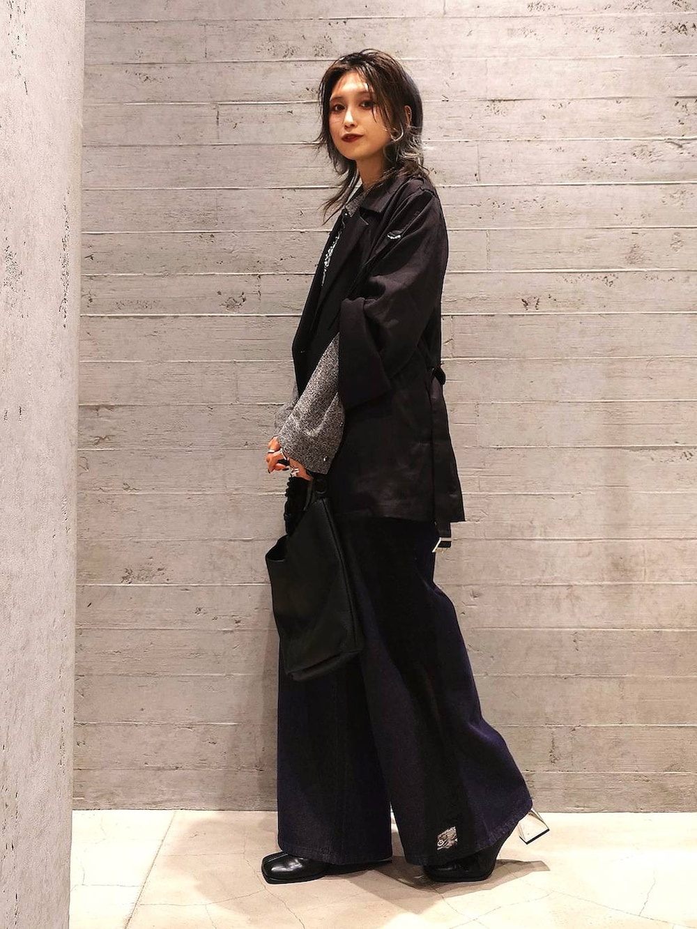 ブラック系のトレンチコート、ブルー系のデニムパンツ、ブラック系のブーツを着用したレディースの秋コーディネートの2枚目の写真