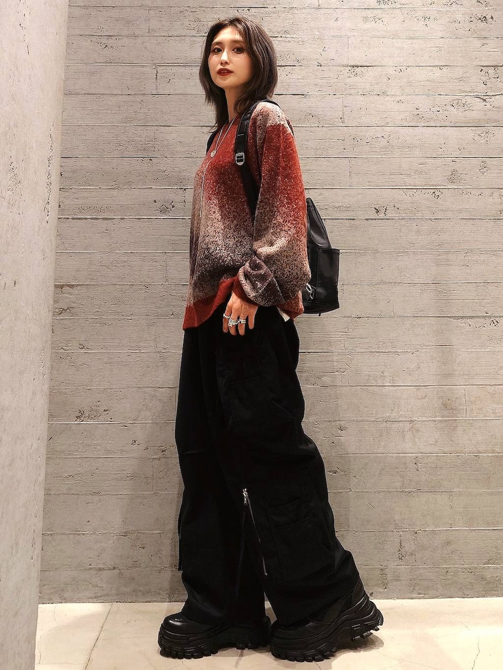 レッド系のニット/セーター、ブラック系のカーゴパンツ、ブラック系のバックパック/リュックを着用したレディースの秋コーディネートの2枚目の写真
