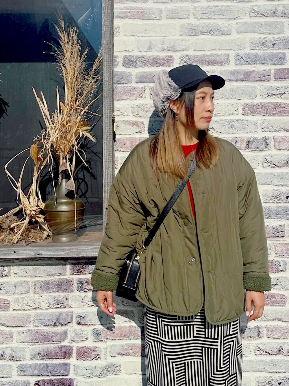 グリーン系のジャケット/アウター、オレンジ系のニット/セーター、その他のスカートを着用したレディースの冬コーディネートの2枚目の写真