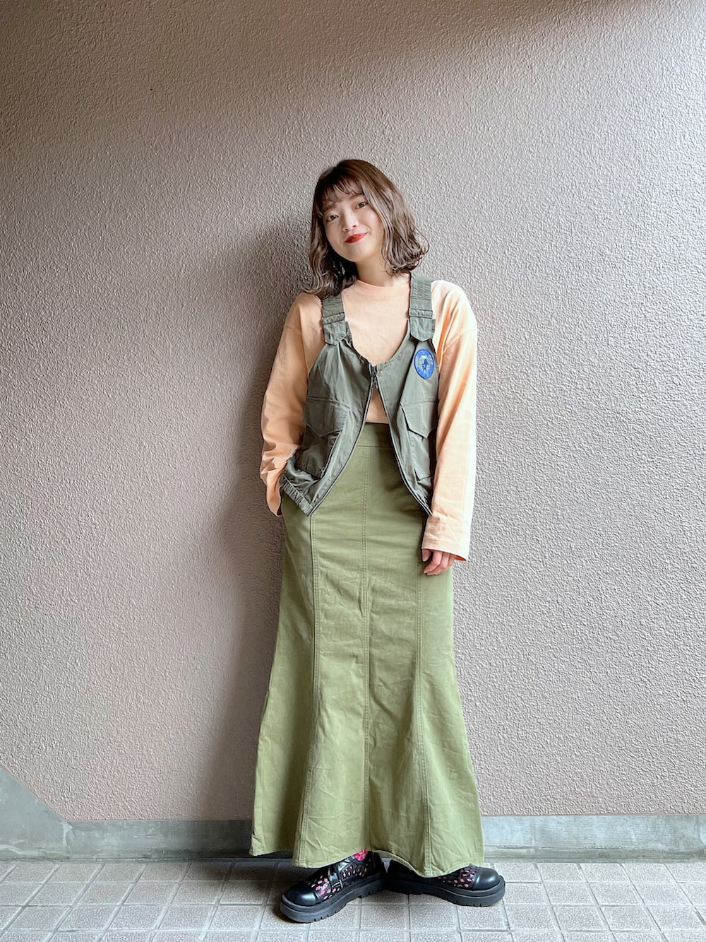 グリーン系のベスト、グリーン系のスカート、ブラック系のその他シューズを着用したレディースの春コーディネートの2枚目の写真