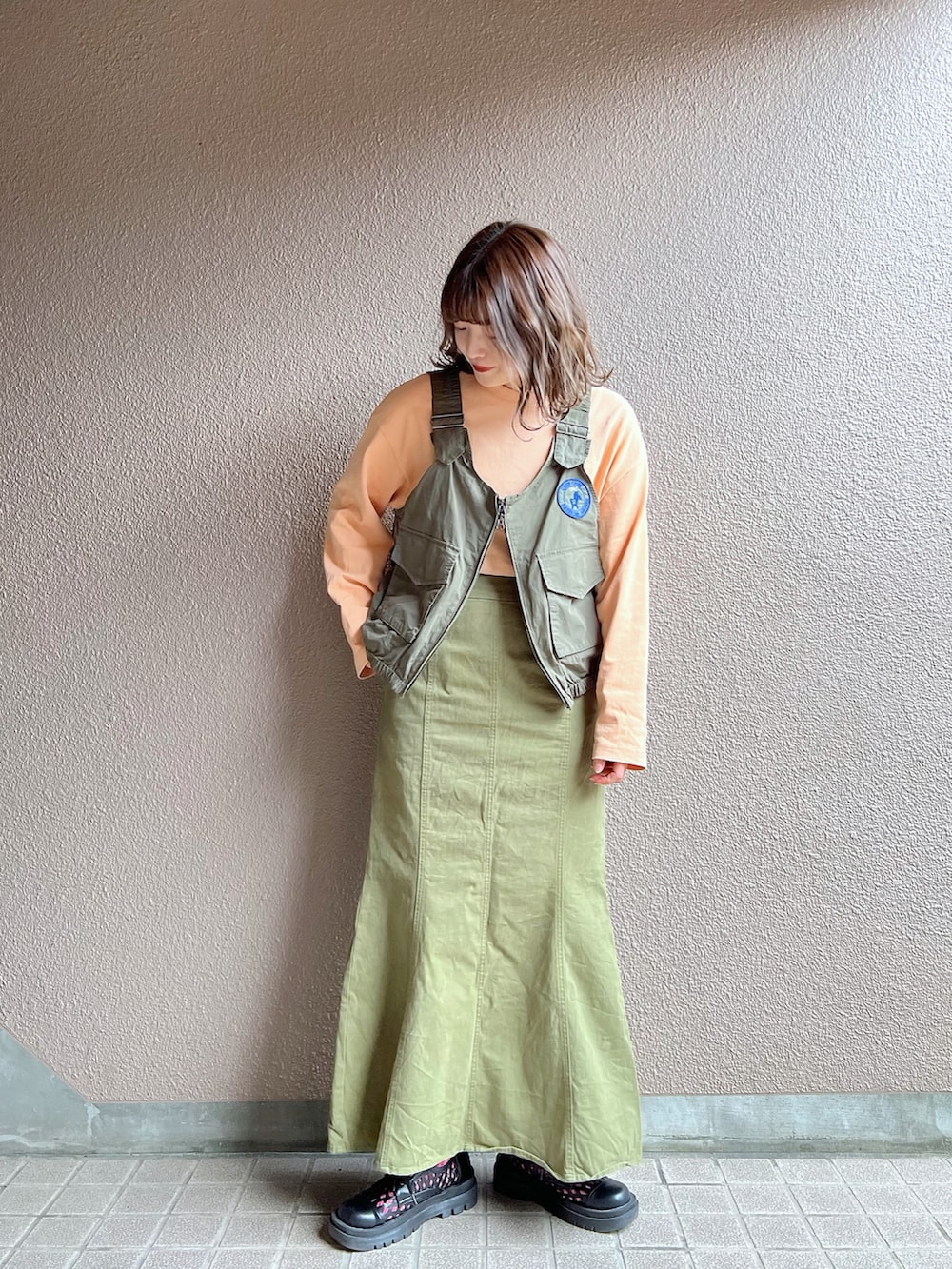 グリーン系のベスト、グリーン系のスカート、ブラック系のその他シューズを着用したレディースの春コーディネートの3枚目の写真