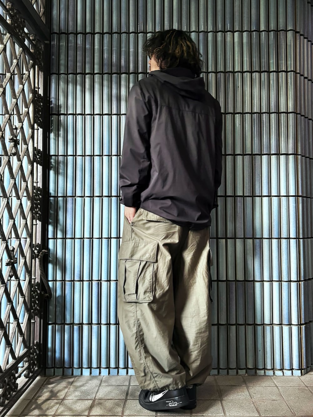 ブラック系のナイロンジャケット、グリーン系のカーゴパンツ、ブラック系のスニーカーを着用したメンズの秋コーディネートの4枚目の写真