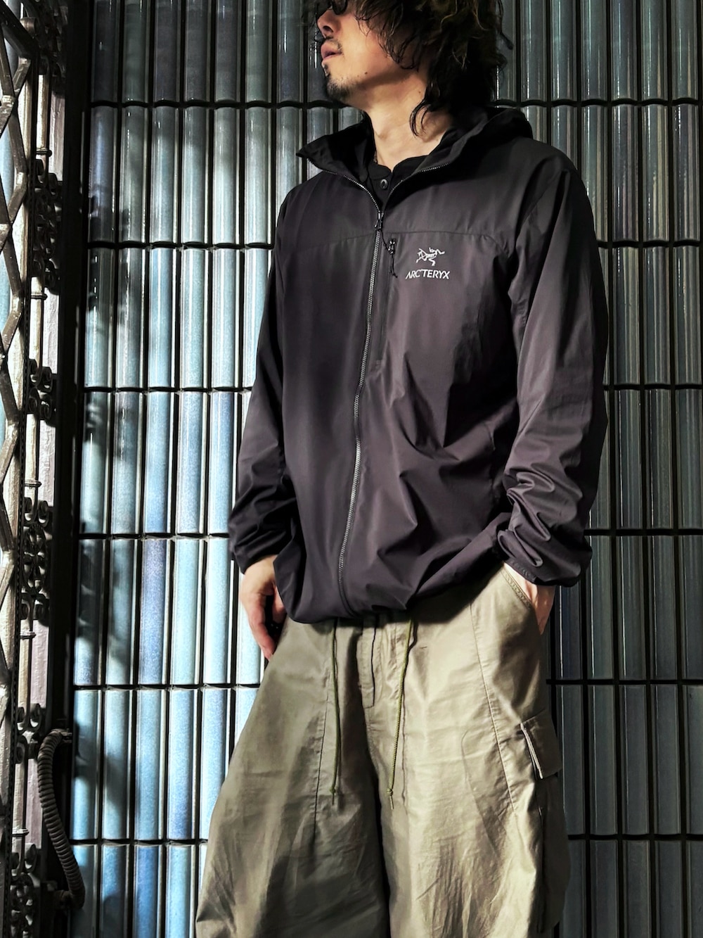 ブラック系のナイロンジャケット、グリーン系のカーゴパンツ、ブラック系のスニーカーを着用したメンズの秋コーディネートの2枚目の写真