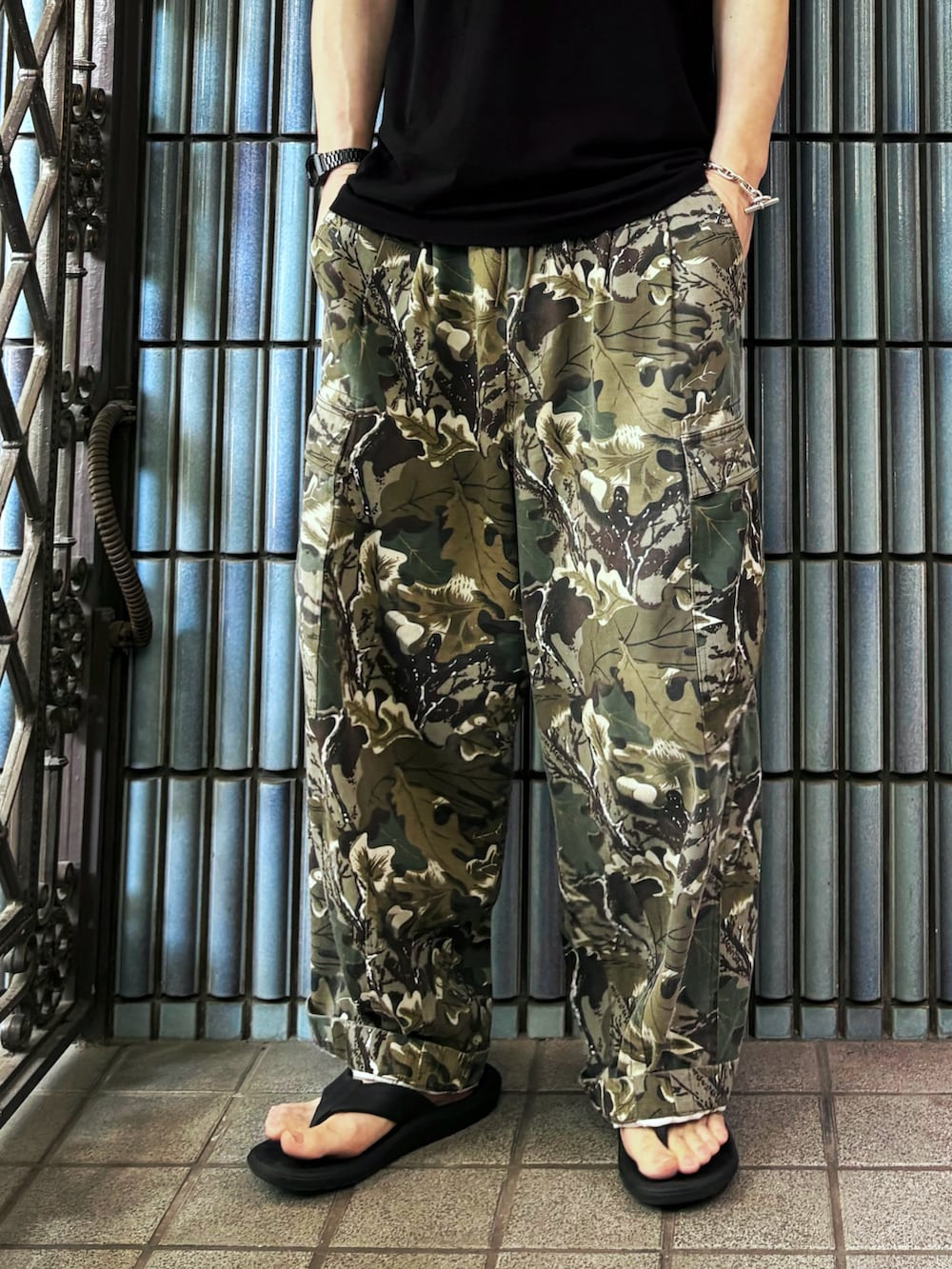 グリーン系のカーゴパンツ、ブラック系のサンダル、ブラック系のTシャツ/カットソーを着用したメンズの夏コーディネートの3枚目の写真