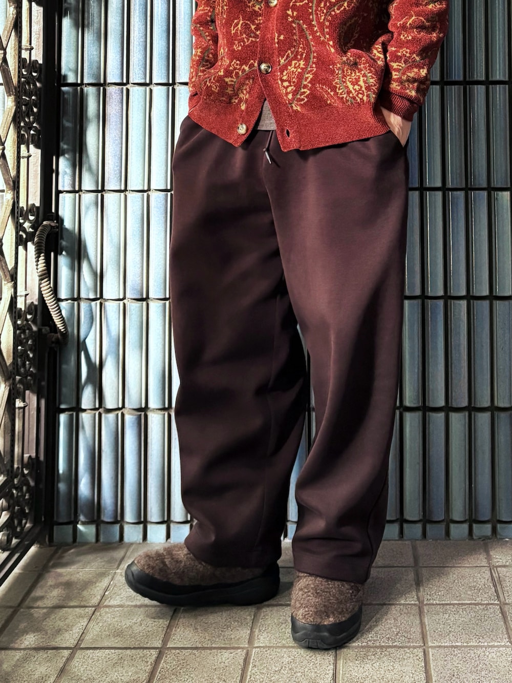 レッド系のカーディガン/ボレロ、ブラウン系のニット/セーター、ブラウン系のスウェットパンツを着用したメンズの冬コーディネートの3枚目の写真