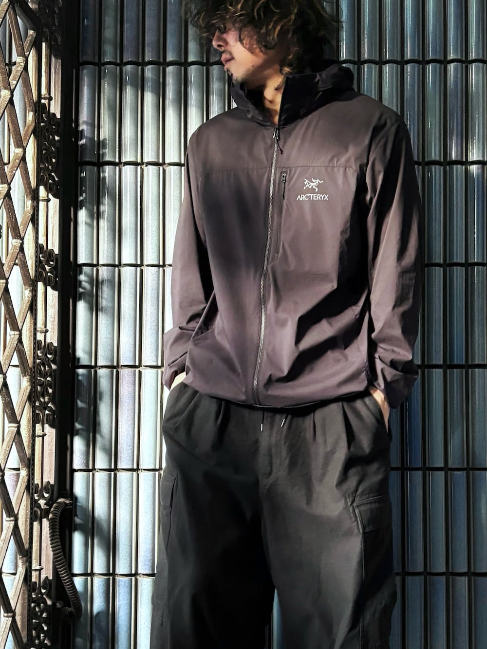 ブラック系のナイロンジャケット、ブラック系のカーゴパンツ、グレー系のスニーカーを着用したメンズの秋コーディネートの2枚目の写真