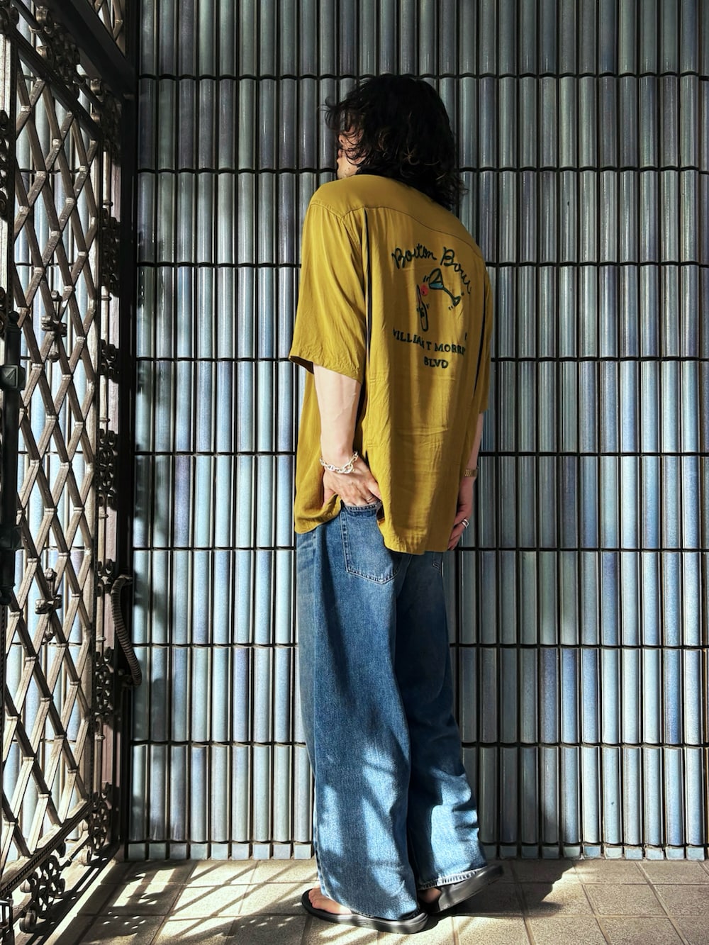 ブラック系のサンダル、イエロー系のシャツ/ブラウス、ブルー系のデニムパンツを着用したメンズの秋コーディネートの4枚目の写真