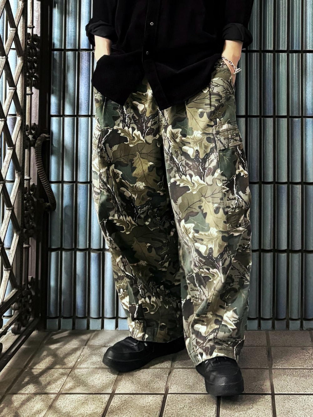 グリーン系のカーゴパンツ、ブラック系のスニーカー、ブラック系のシャツ/ブラウスを着用したメンズの春コーディネートの3枚目の写真