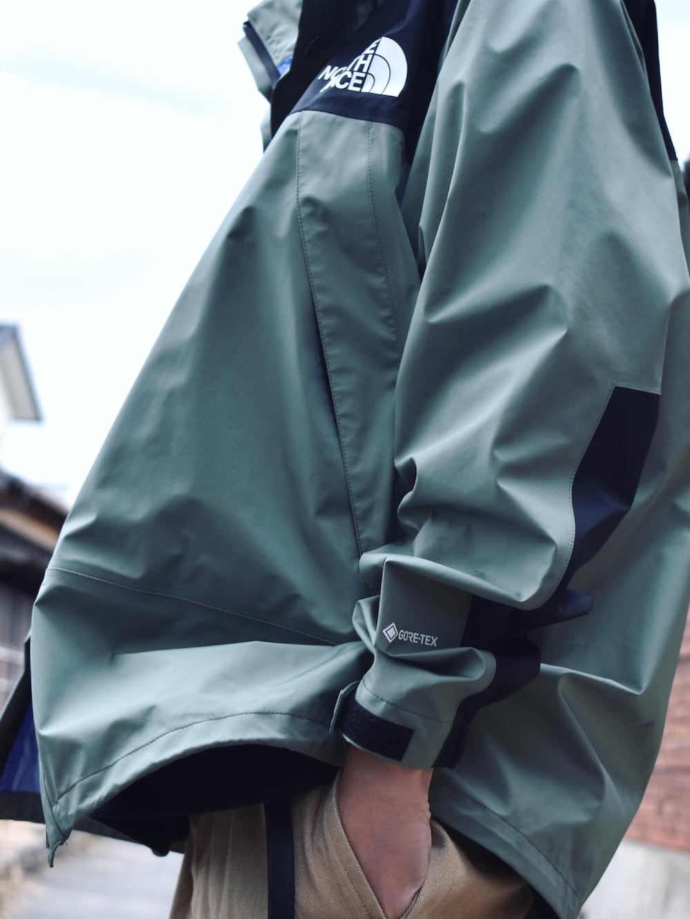 グリーン系のマウンテンパーカー、ブラック系のスウェット、グリーン系のチノパンツを着用したメンズの冬コーディネートの2枚目の写真