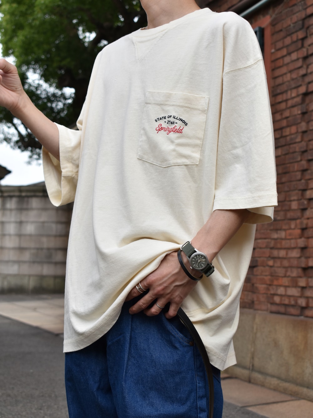 ベージュ系のTシャツ/カットソー、ブルー系のデニムパンツ、ブラック系のサンダルを着用したメンズの夏コーディネートの2枚目の写真