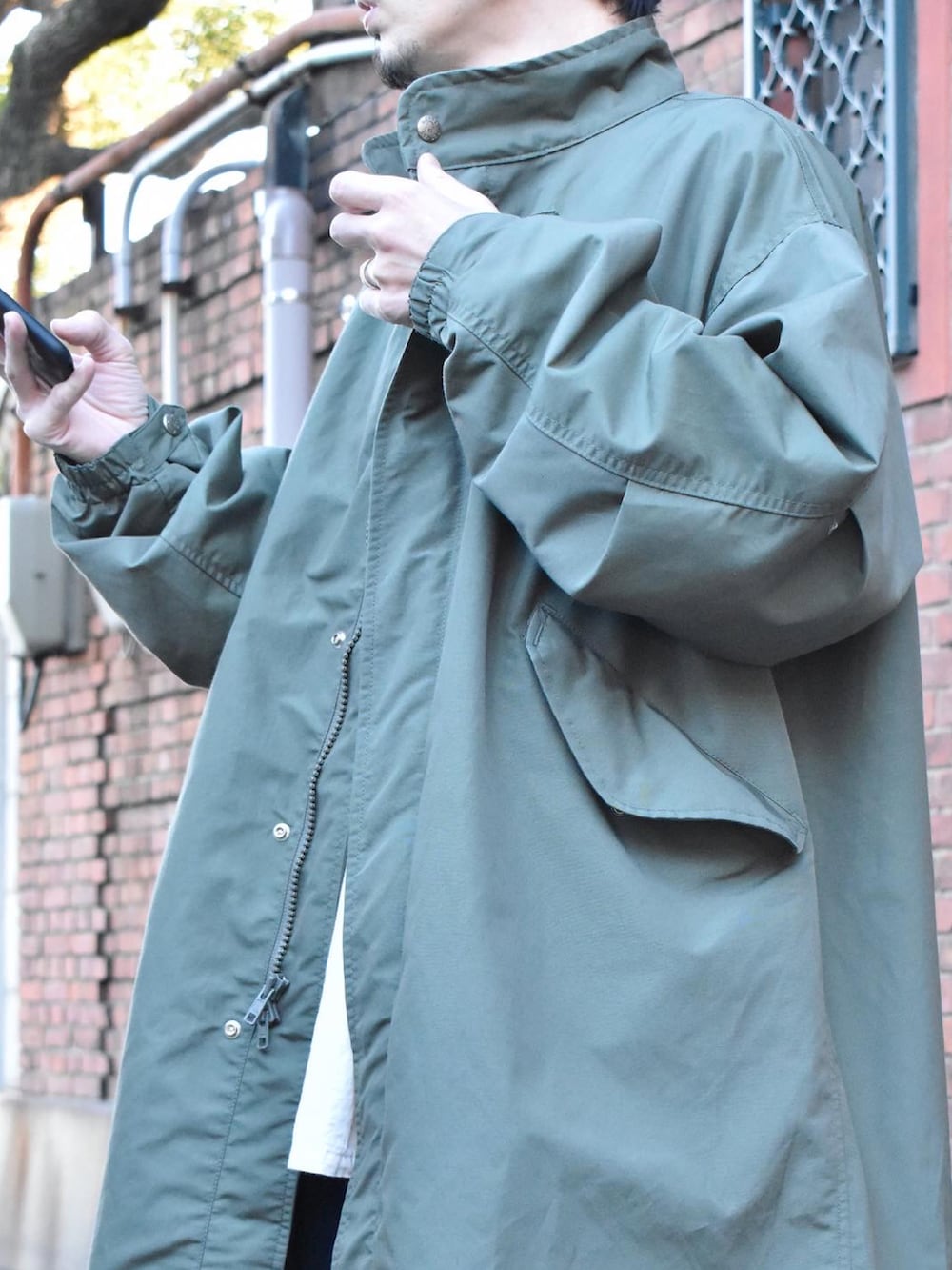 グリーン系のノーカラーコート、ホワイト系のシャツ/ブラウス、ブルー系のデニムパンツを着用したメンズの冬コーディネートの2枚目の写真