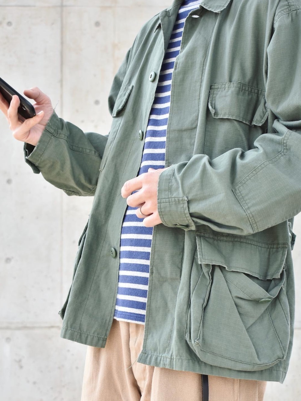 グリーン系のミリタリージャケット、グリーン系のチノパンツ、ブラック系のシューズを着用したメンズの秋コーディネートの2枚目の写真