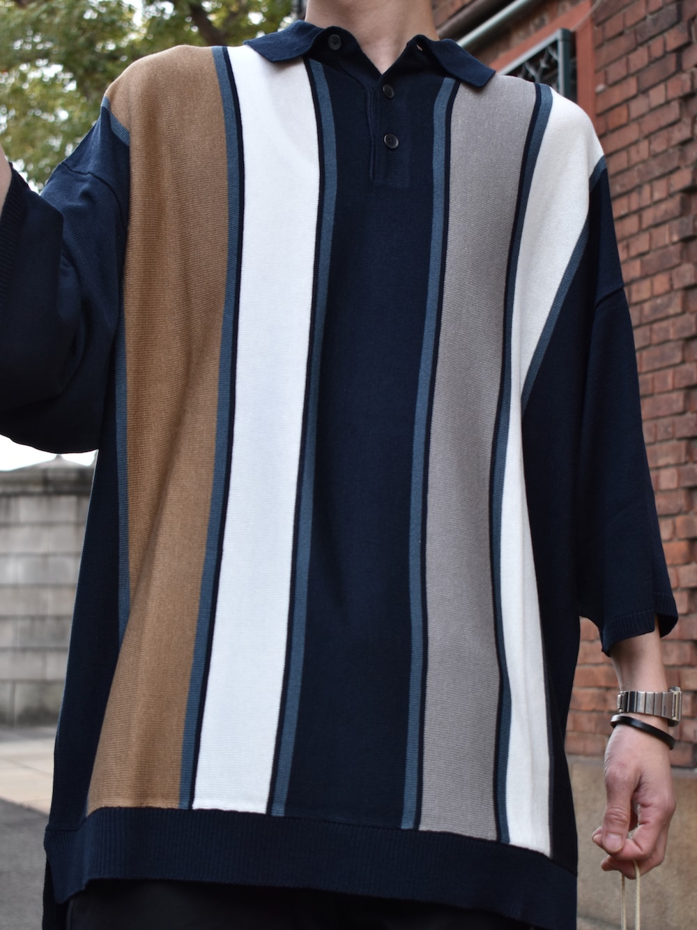 ブルー系のポロシャツ、グレー系のチノパンツ、ベージュ系のハンドバッグを着用したメンズの春コーディネートの2枚目の写真