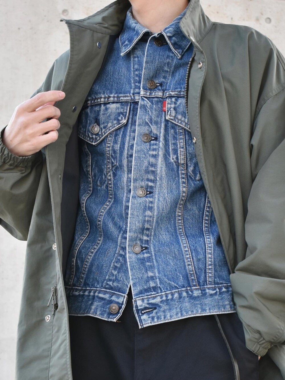 グリーン系のノーカラーコート、ブルー系のデニムジャケット、グレー系のチノパンツを着用したメンズの冬コーディネートの2枚目の写真