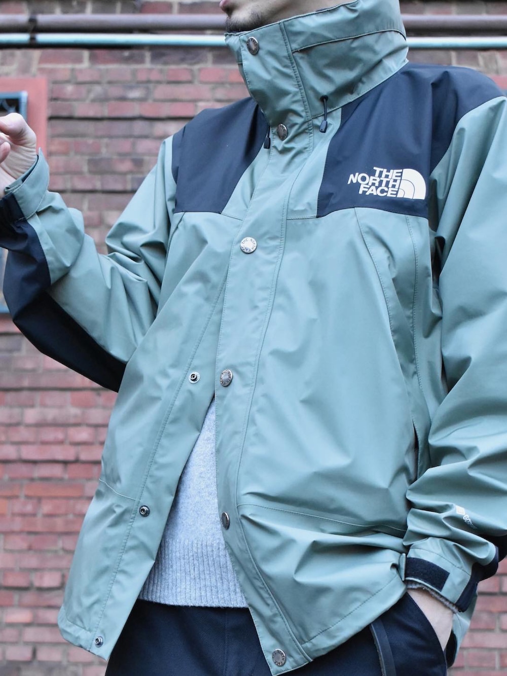 グリーン系のマウンテンパーカー、グレー系のチノパンツ、ブラック系のシューズを着用したメンズの冬コーディネートの2枚目の写真