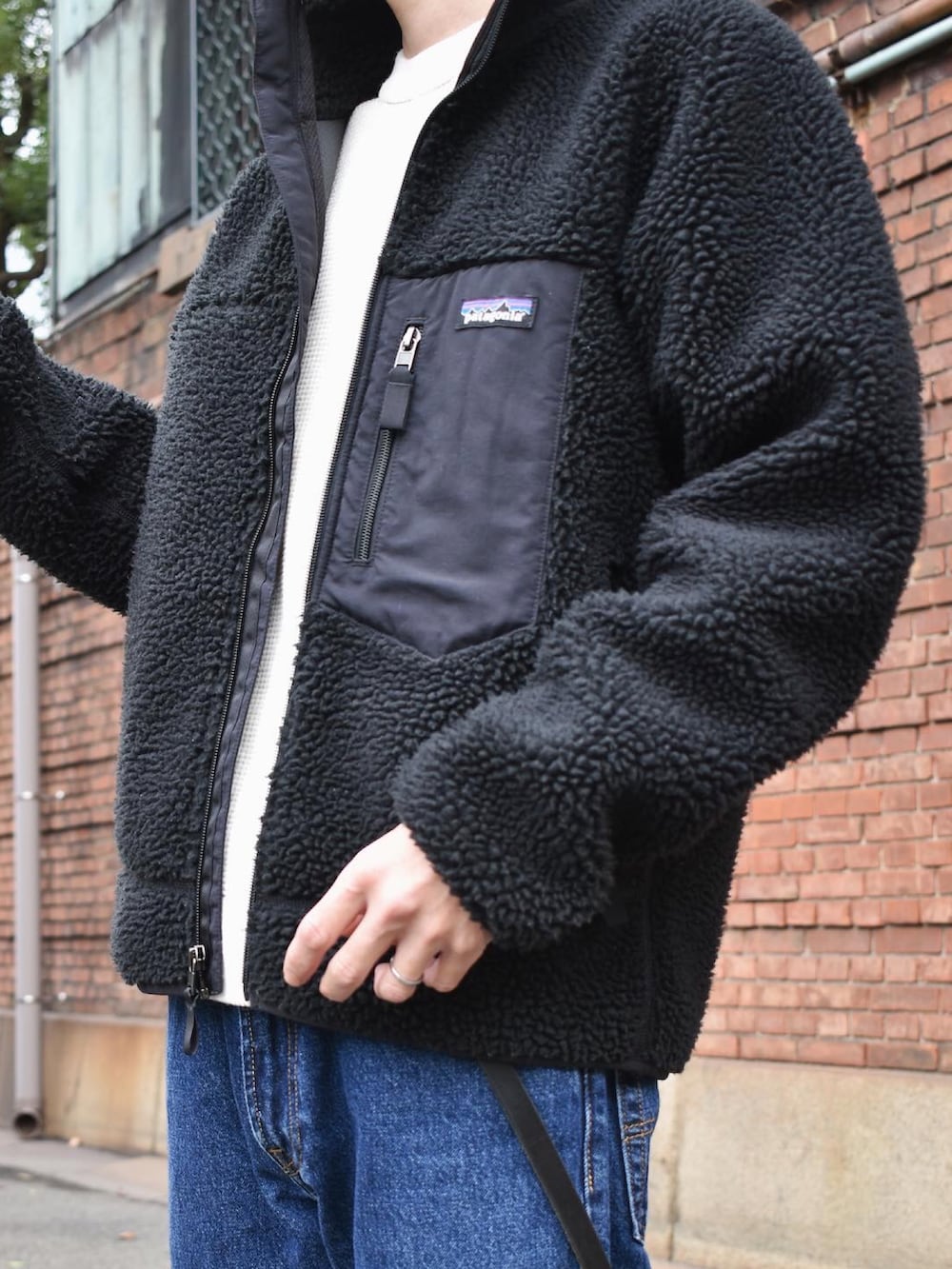 ブラック系のブルゾン、ホワイト系のニット/セーター、ブルー系のデニムパンツを着用したメンズの秋コーディネートの2枚目の写真