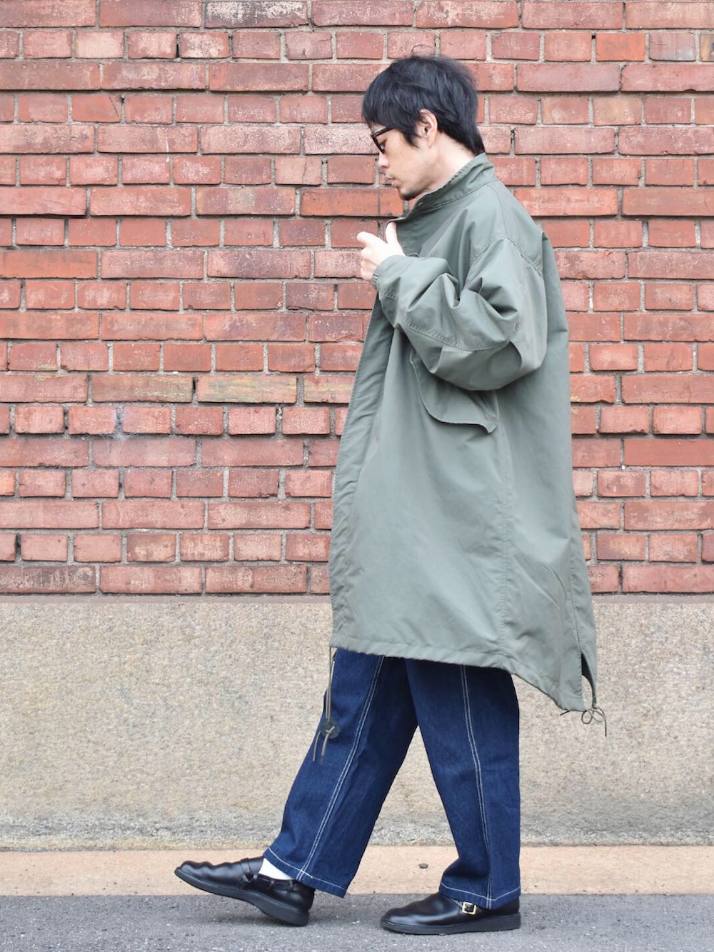 グリーン系のノーカラーコート、ブラック系のTシャツ/カットソー、ブルー系のデニムパンツを着用したメンズの秋コーディネートの2枚目の写真