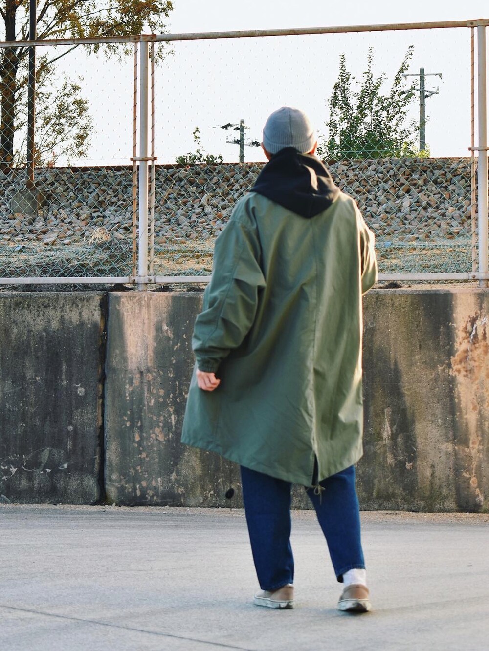 グリーン系のノーカラーコート、ブルー系のデニムパンツ、グレー系のスニーカーを着用したメンズの秋コーディネートの2枚目の写真