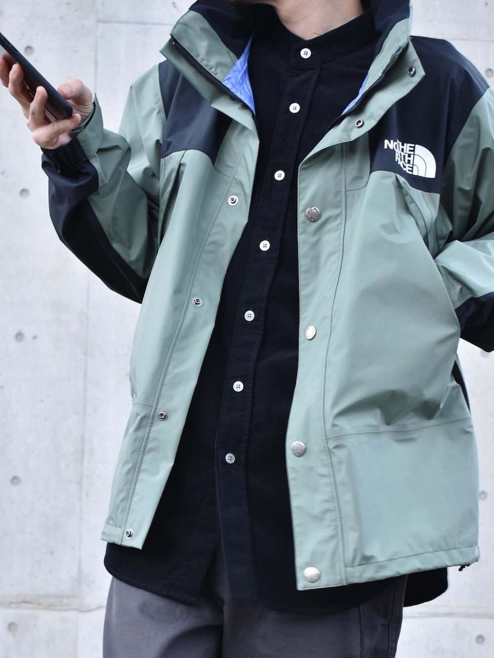 グリーン系のマウンテンパーカー、ブラック系のシャツ/ブラウス、グレー系のチノパンツを着用したメンズの秋コーディネートの2枚目の写真