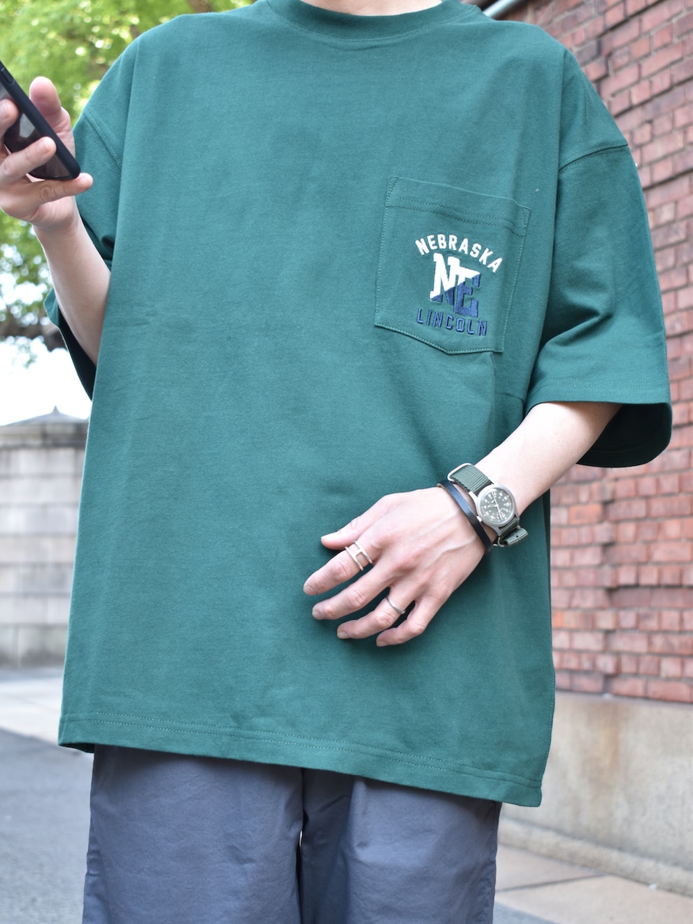 グリーン系のTシャツ/カットソー、グレー系のパンツ、ブラック系のサンダルを着用したメンズの春コーディネートの3枚目の写真