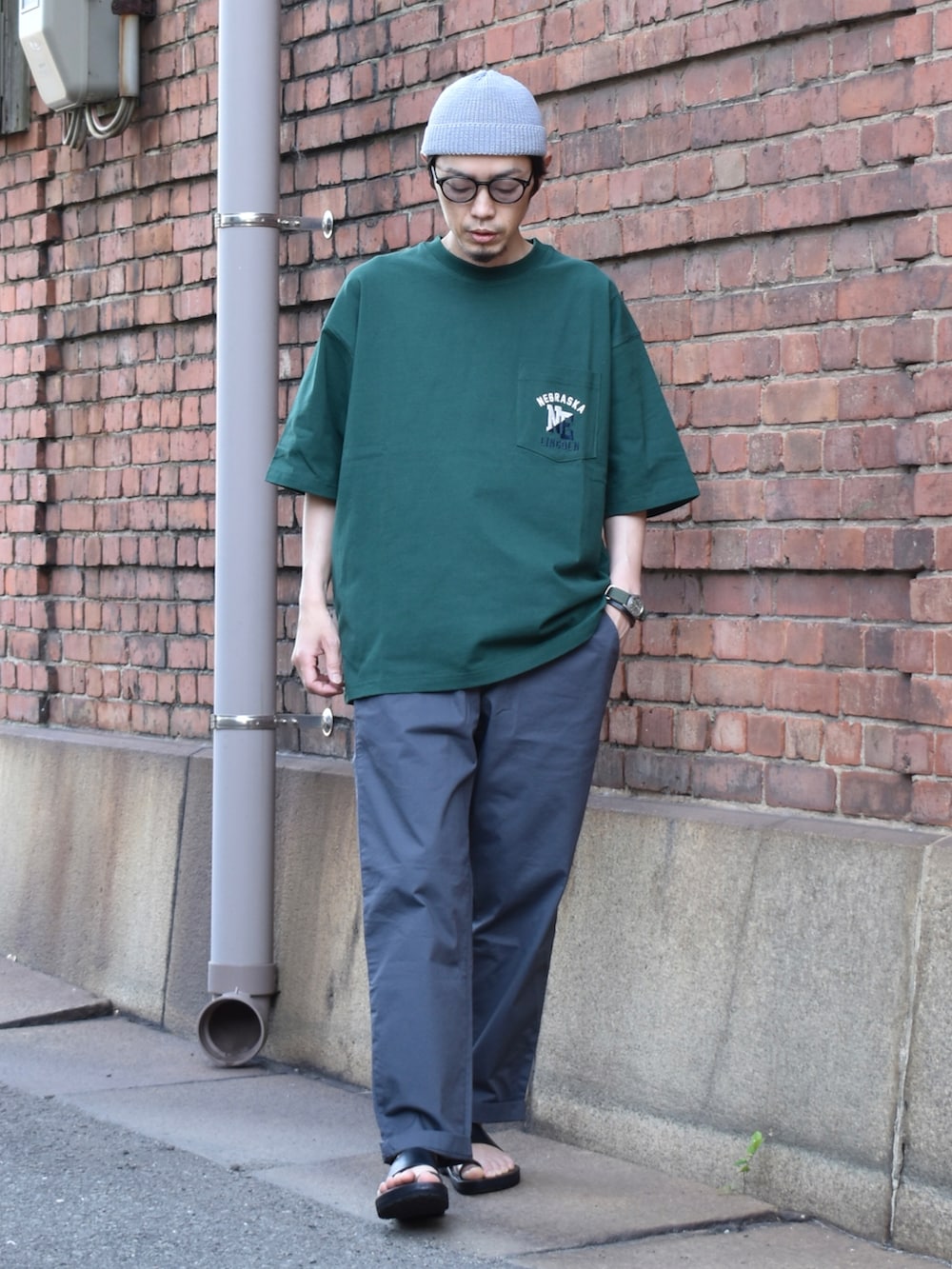 グリーン系のTシャツ/カットソー、グレー系のパンツ、ブラック系のサンダルを着用したメンズの春コーディネートの2枚目の写真