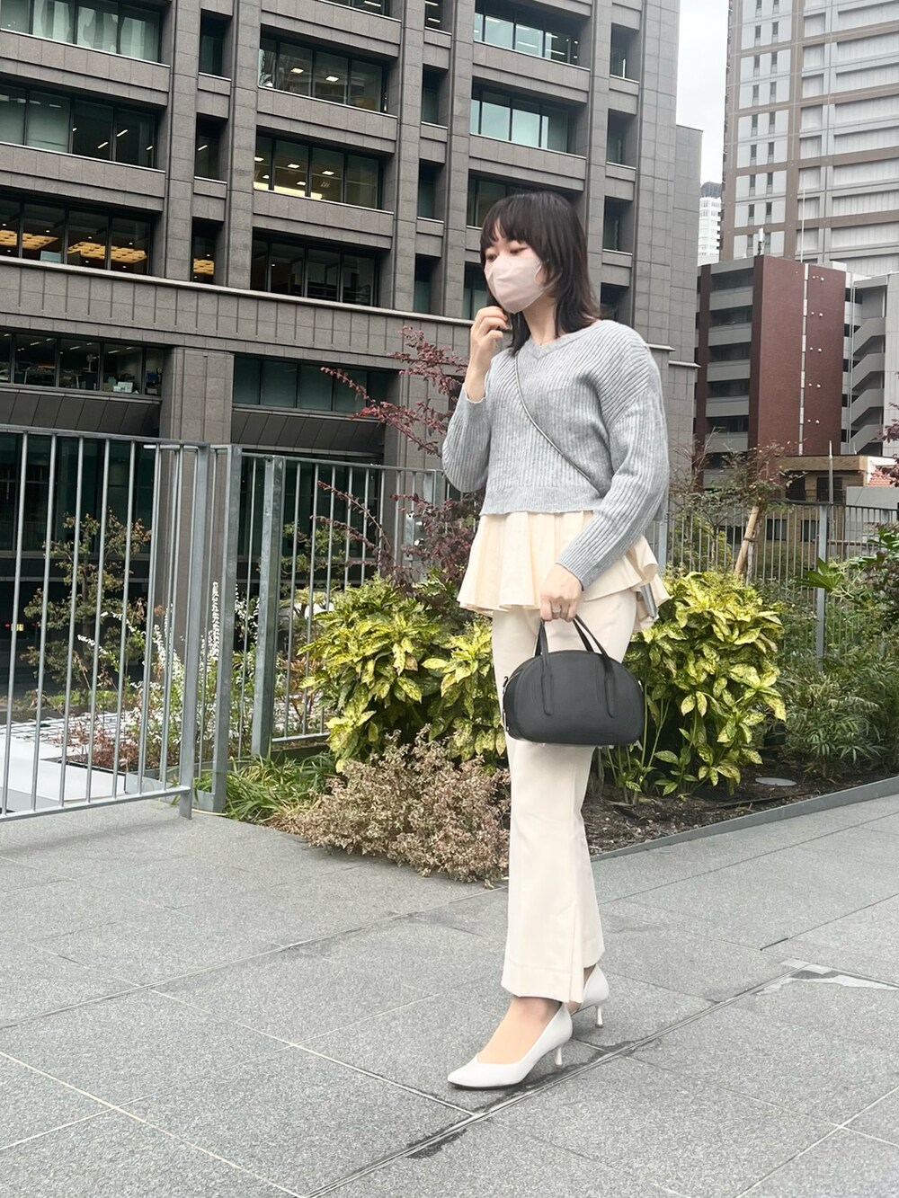 ブラック系のバッグ、グレー系のトップス、ホワイト系のパンプスを着用したレディースの春コーディネートの2枚目の写真