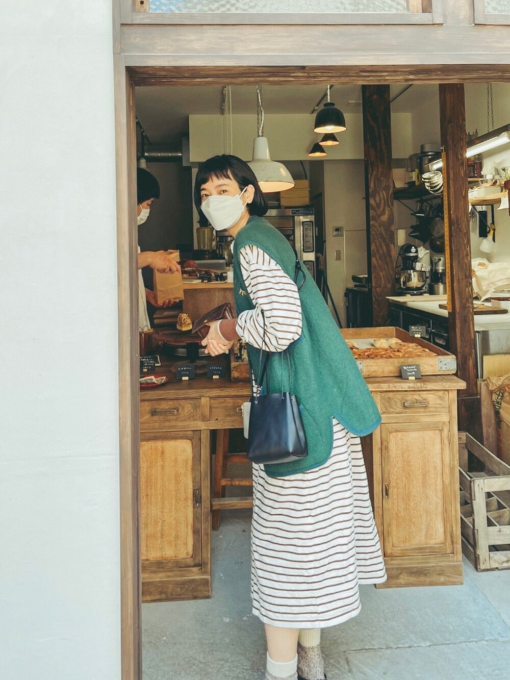 ブラウン系のワンピース、グリーン系のベスト、ブラック系のドレスシューズを着用したレディースの春コーディネートの2枚目の写真