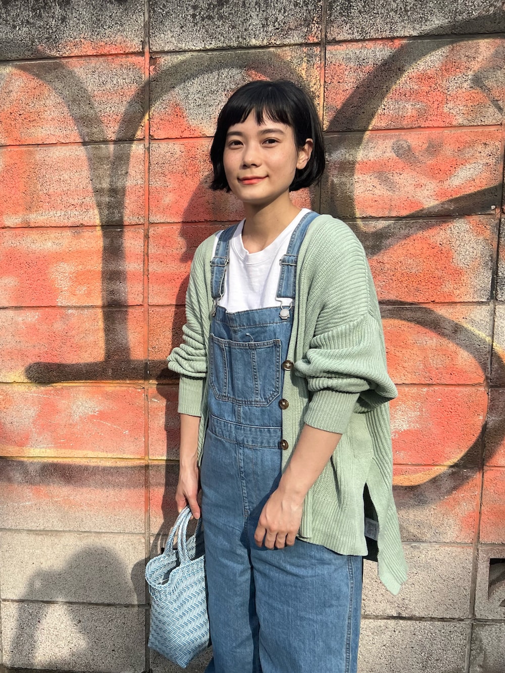 グリーン系のカーディガン/ボレロ、ブルー系のサロペット/オーバーオール、ブルー系のかごバッグを着用したレディースの春コーディネートの5枚目の写真