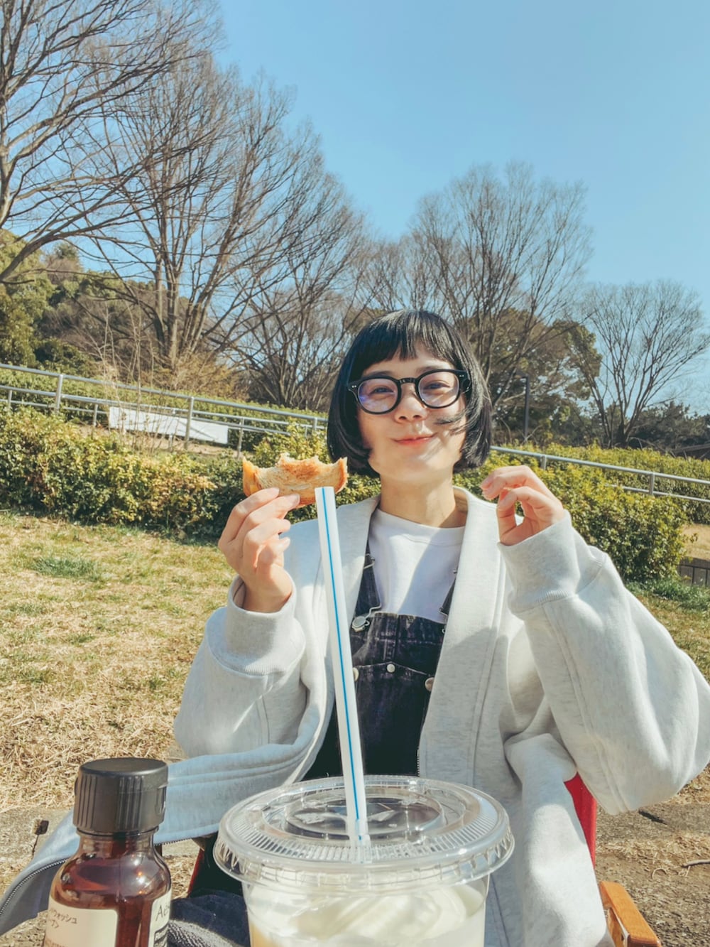 ベージュ系のトレンチコート、ブラック系のオールインワン・サロペット、ホワイト系のスウェットを着用したレディースの春コーディネートの2枚目の写真