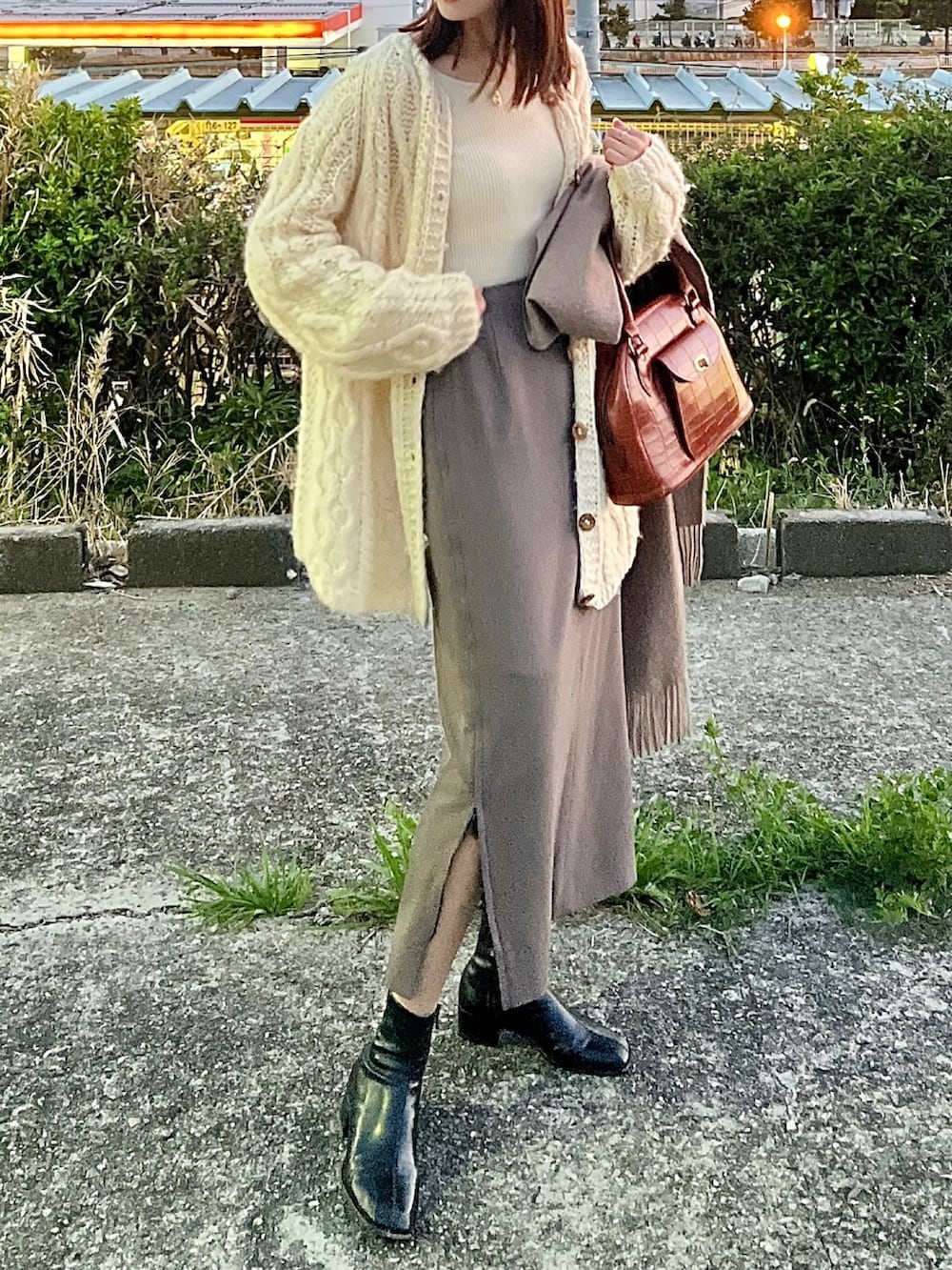 ベージュ系のトップス、ブラウン系のバッグ、ブラック系のブーツを着用したレディースの春コーディネートの2枚目の写真