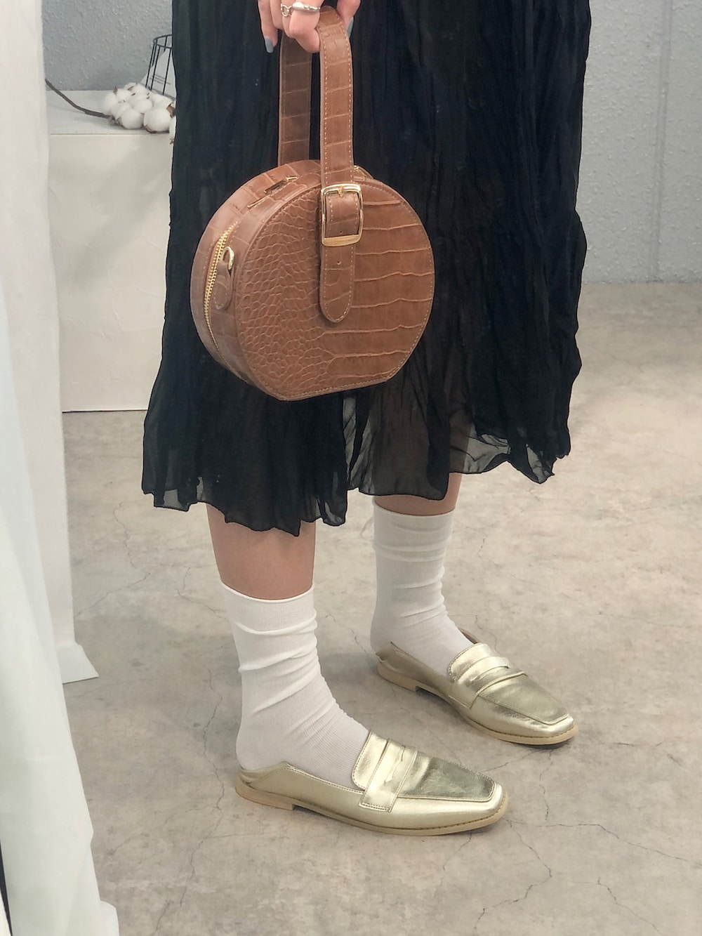 ブラウン系のハンドバッグ、ゴールド系のローファー、ホワイト系のレッグウェアを着用したレディースの秋コーディネートの2枚目の写真
