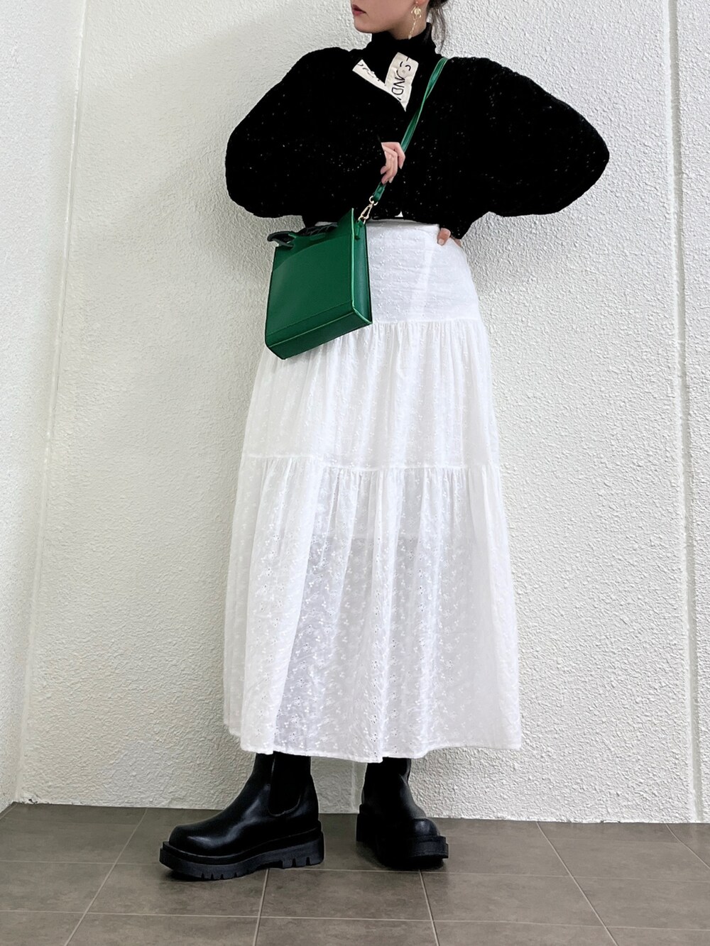 ホワイト系のスカート、グリーン系のショルダーバッグ、ブラック系のブーツを着用したレディースの冬コーディネートの2枚目の写真