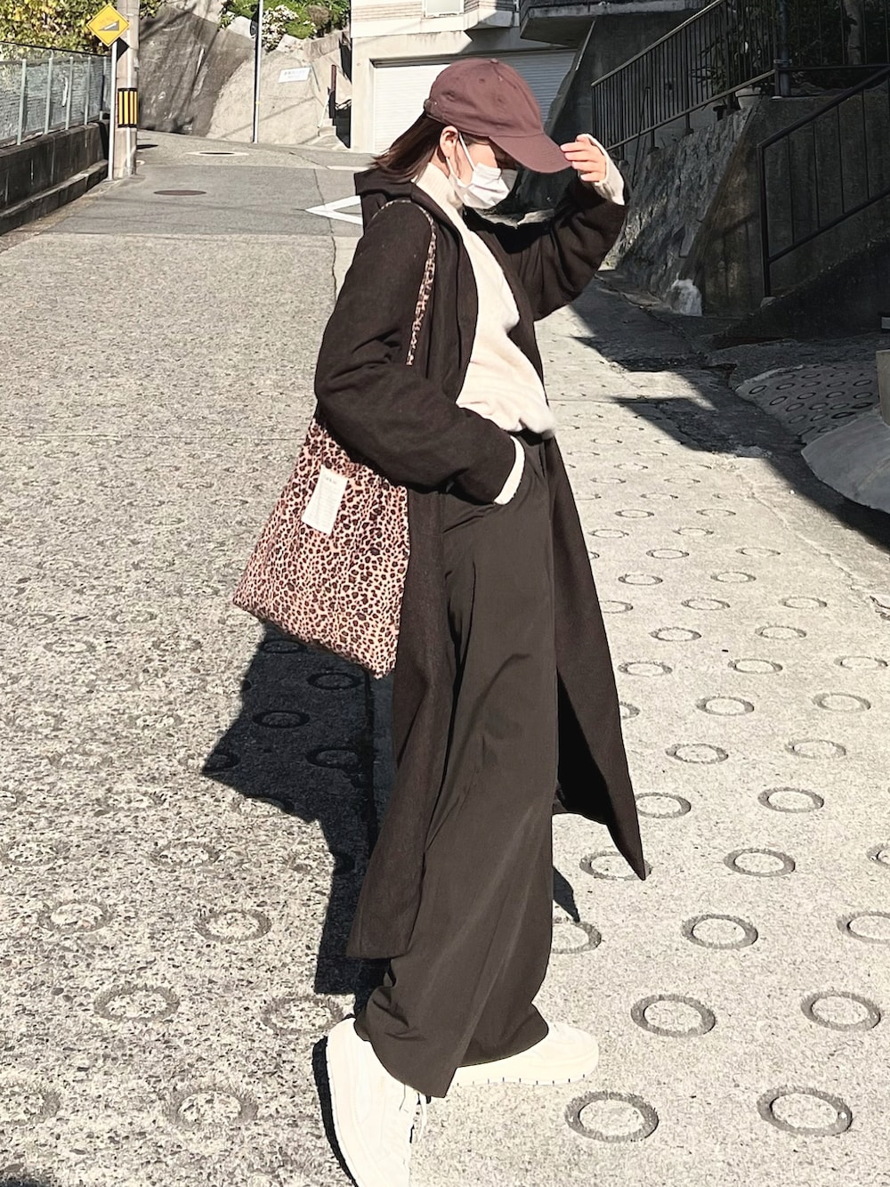 ブラウン系のチェスターコート、ブラウン系のパンツ、その他のトートバッグを着用したレディースの冬コーディネートの3枚目の写真