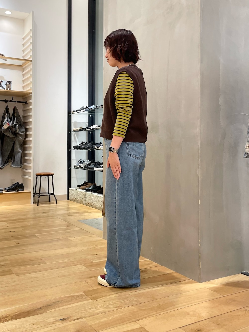 ブルー系のデニムパンツ、ブラウン系のベスト、イエロー系のTシャツ/カットソーを着用したレディースの秋コーディネートの2枚目の写真