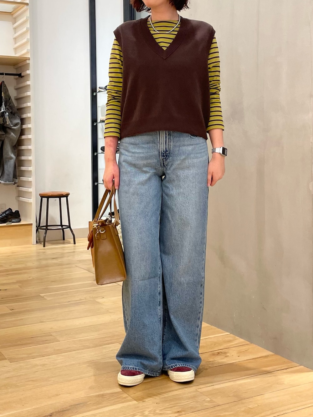 ブルー系のデニムパンツ、ブラウン系のベスト、イエロー系のTシャツ/カットソーを着用したレディースの秋コーディネートの4枚目の写真