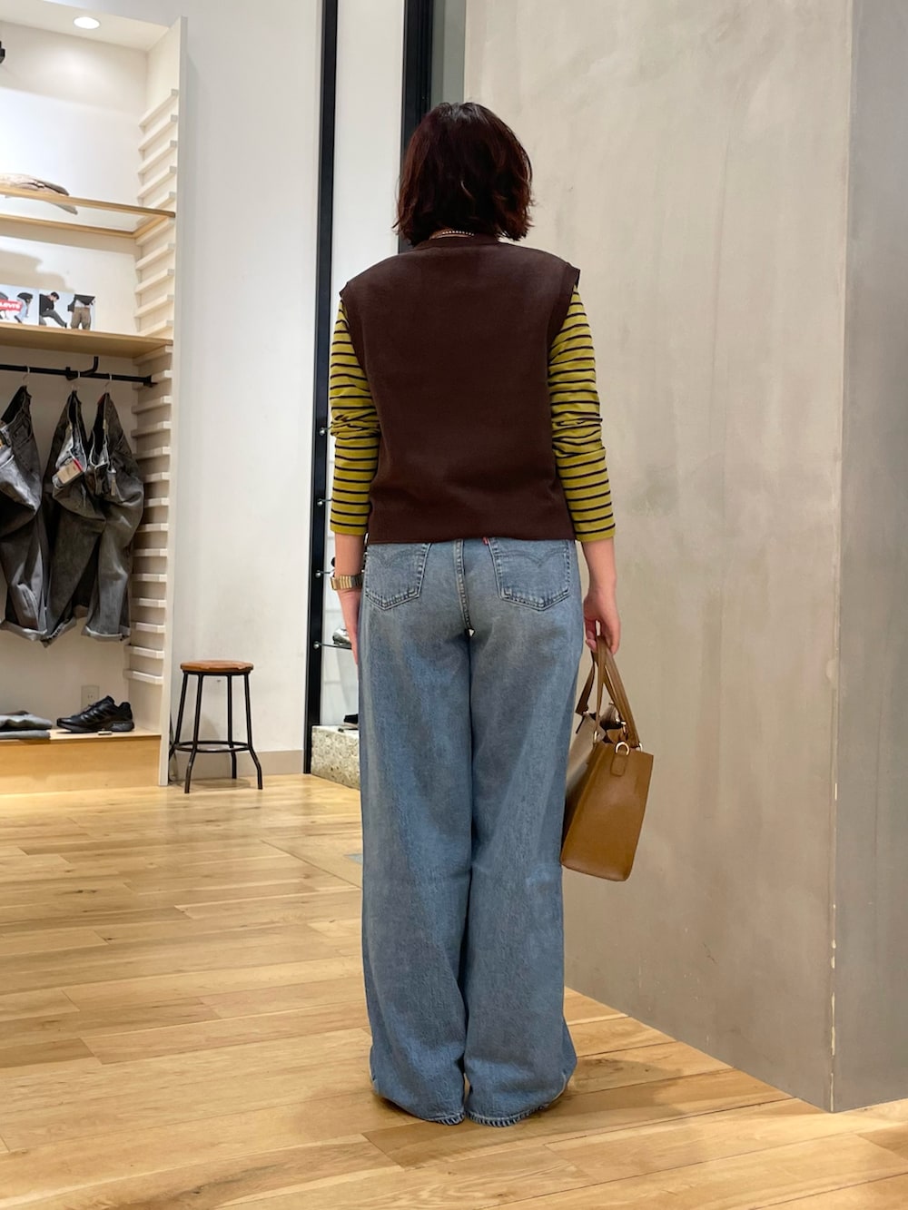 ブルー系のデニムパンツ、ブラウン系のベスト、イエロー系のTシャツ/カットソーを着用したレディースの秋コーディネートの3枚目の写真
