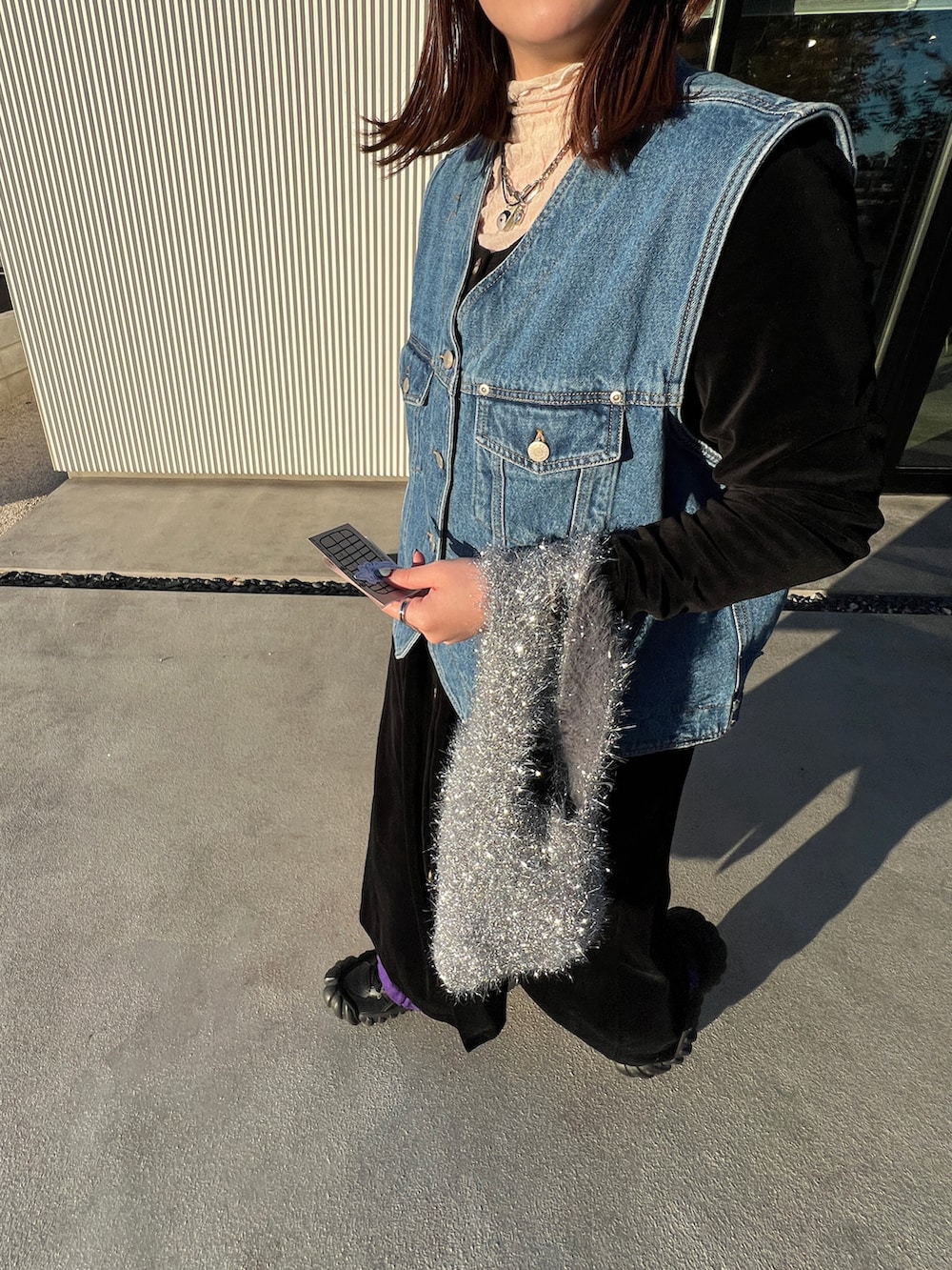 ブルー系のベスト、ブラック系のワンピース/ドレス、シルバー系のハンドバッグを着用したレディースの冬コーディネートの2枚目の写真