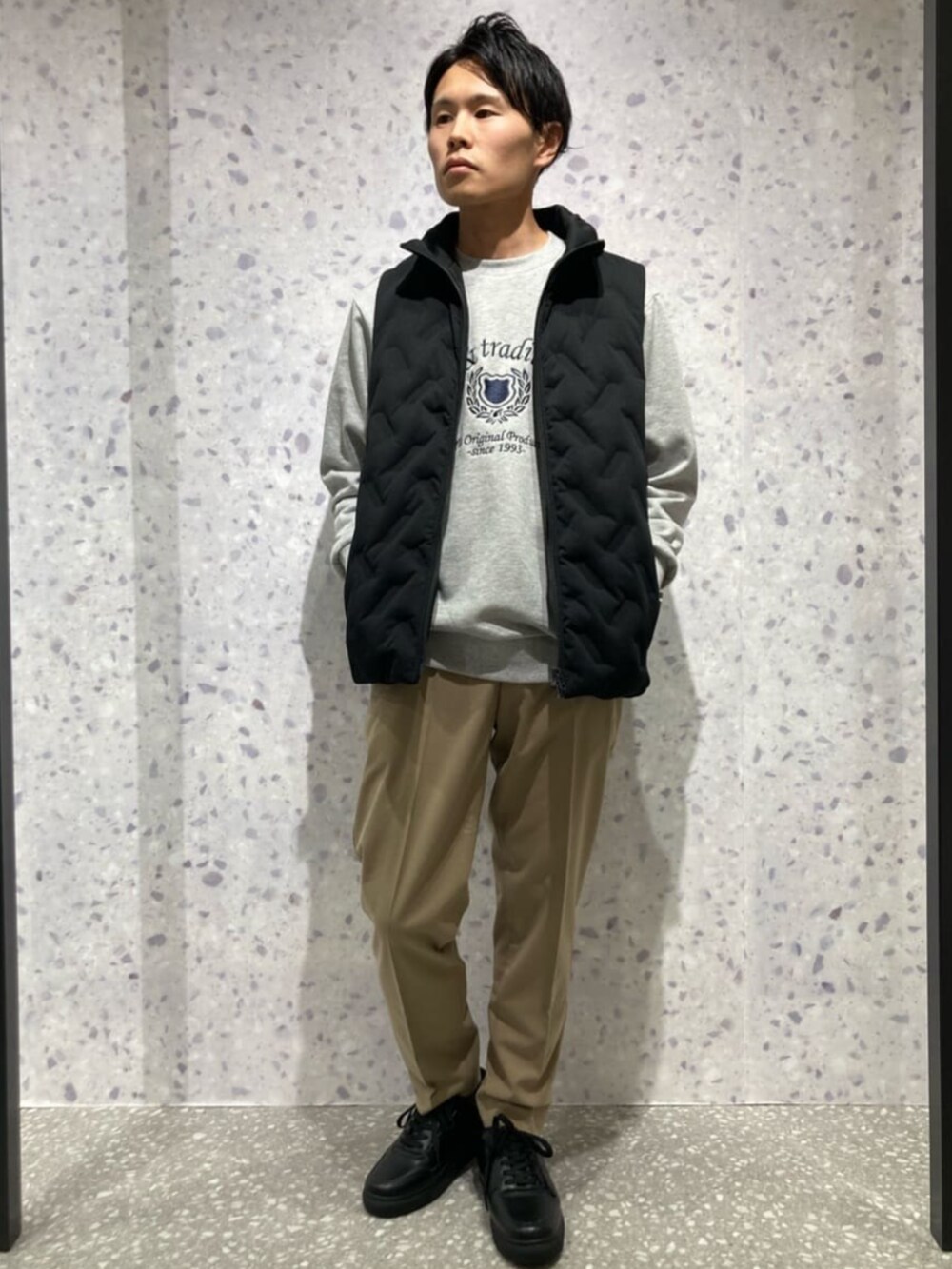 ブラック系のダウンベスト、グレー系のTシャツ/カットソー、ベージュ系のスラックスを着用したメンズの秋コーディネートの3枚目の写真