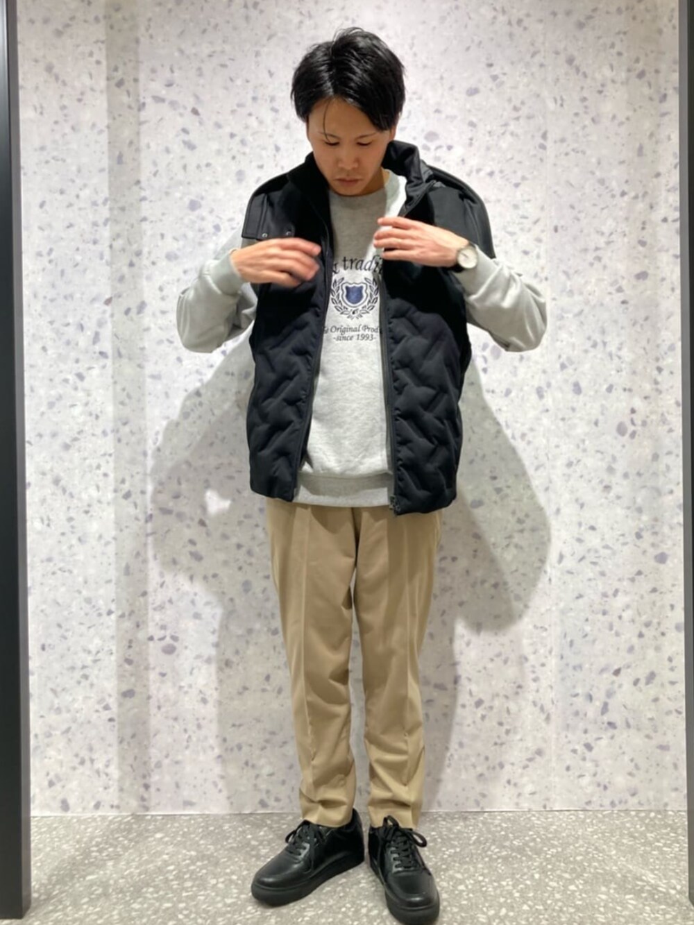 ブラック系のダウンベスト、グレー系のTシャツ/カットソー、ベージュ系のスラックスを着用したメンズの秋コーディネートの2枚目の写真