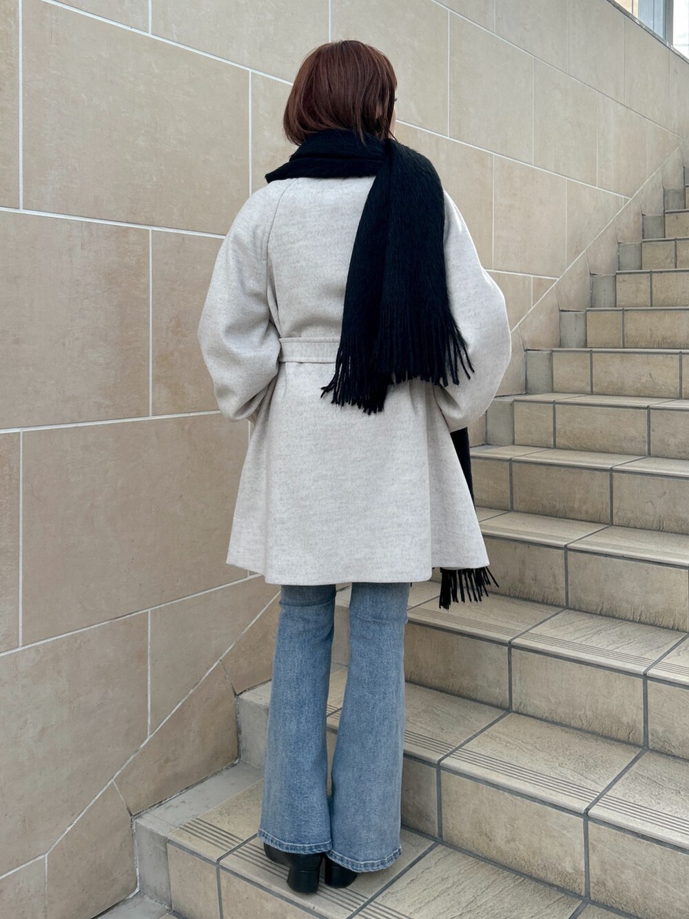 ベージュ系のステンカラーコート、ブルー系のデニムパンツ、ブラック系のマフラーを着用したレディースの冬コーディネートの2枚目の写真