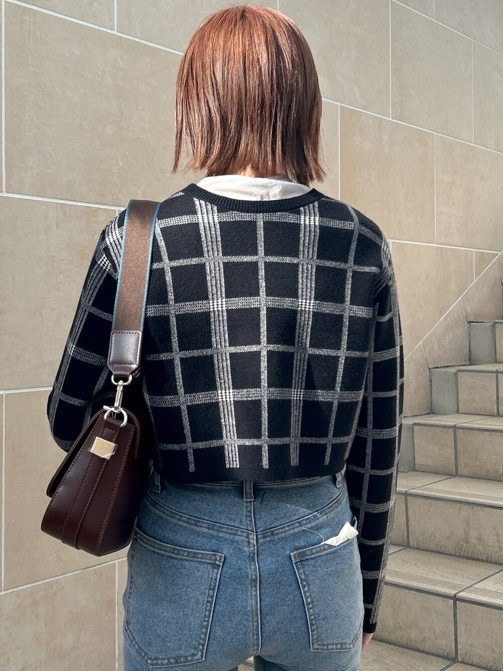 ブラウン系のショルダーバッグ、ブルー系のデニムパンツ、ブラック系のニット/セーターを着用したレディースの冬コーディネートの5枚目の写真