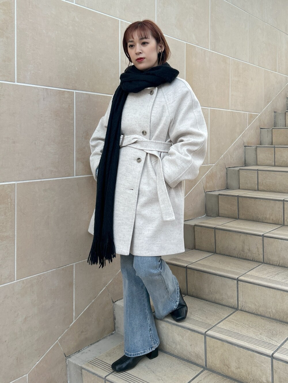 ベージュ系のステンカラーコート、ブルー系のデニムパンツ、ブラック系のマフラーを着用したレディースの冬コーディネートの3枚目の写真