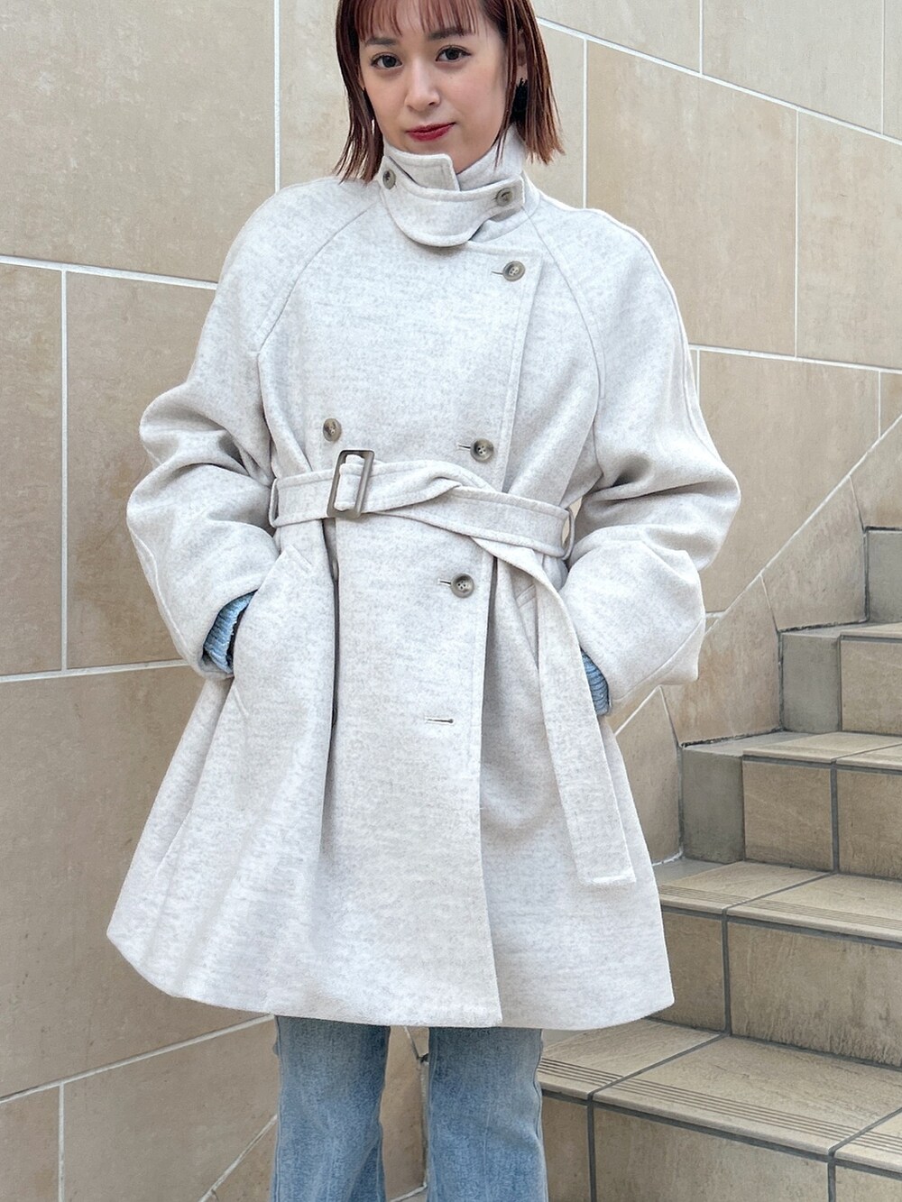 ベージュ系のステンカラーコート、ブルー系のデニムパンツ、ブラック系のマフラーを着用したレディースの冬コーディネートの5枚目の写真