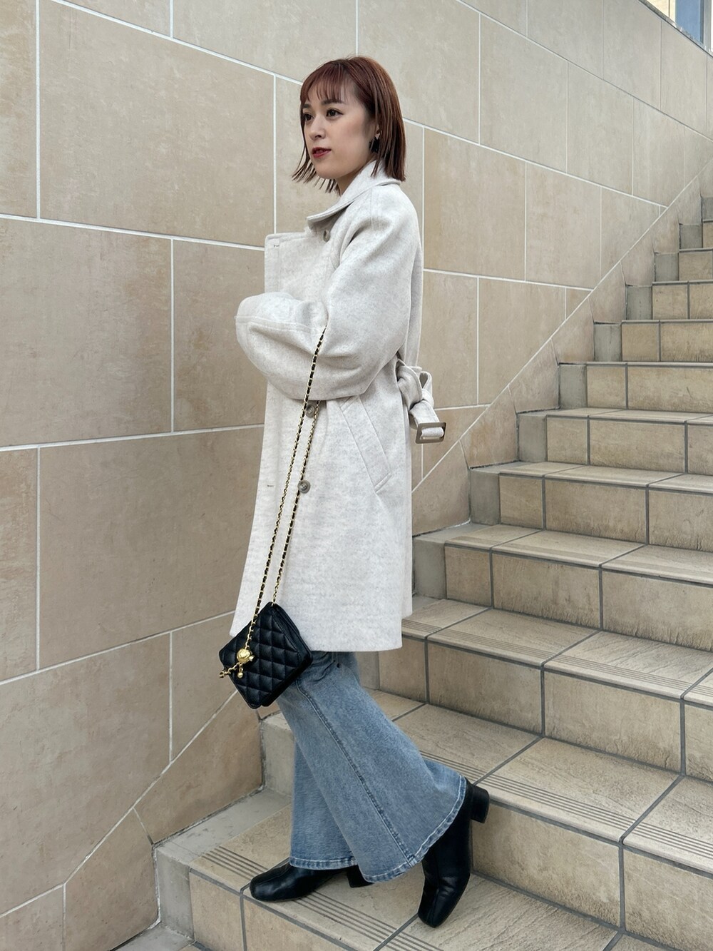 ブルー系のデニムパンツ、ブルー系のニット/セーター、ベージュ系のステンカラーコートを着用したレディースの冬コーディネートの2枚目の写真