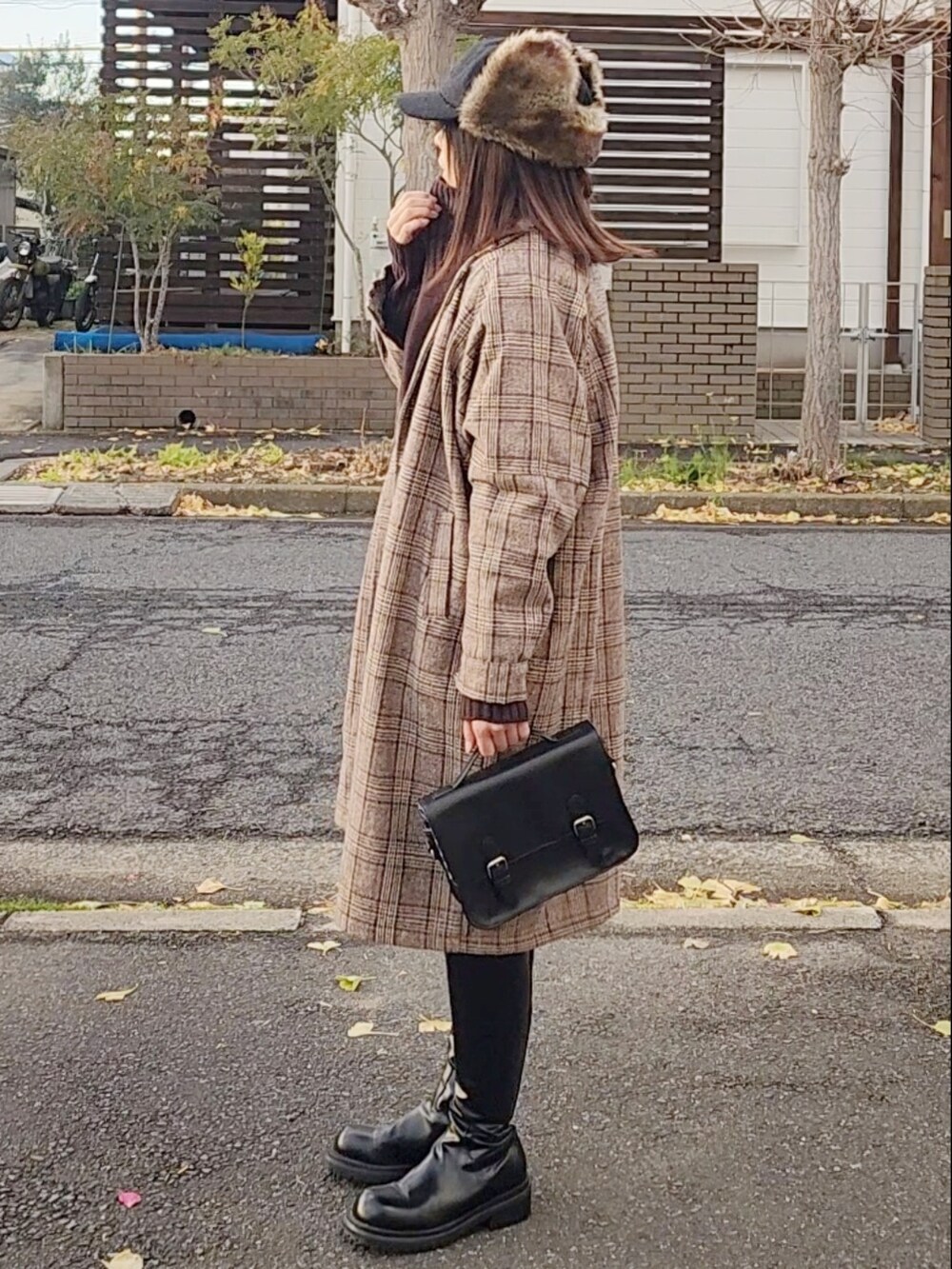 ブラウン系のチェスターコート、ブラウン系のニット/セーター、ブラック系のショルダーバッグを着用したレディースの冬コーディネートの2枚目の写真