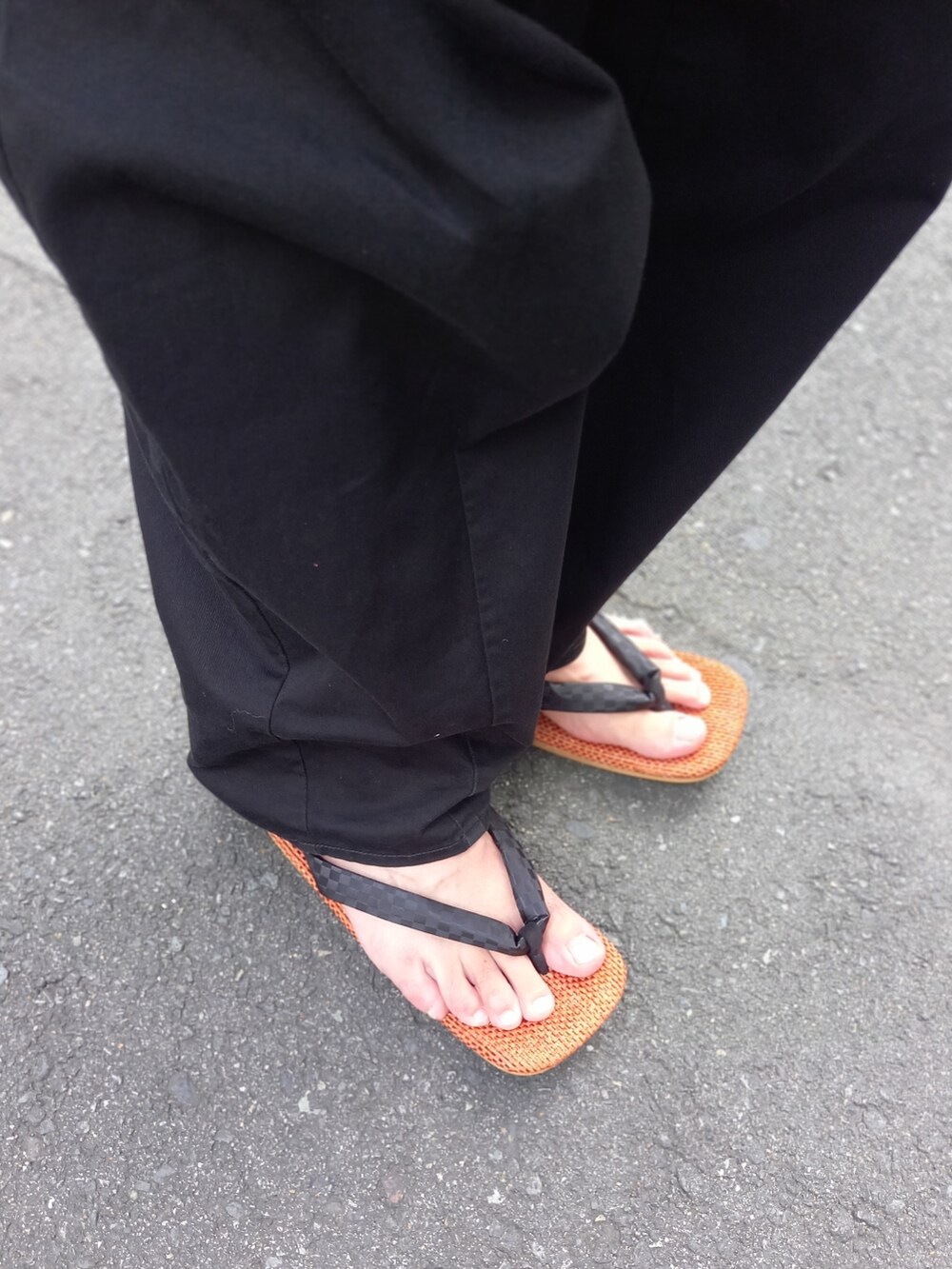 オレンジ系のサンダル、ブラック系のトップス、ブラック系のパンツを着用したメンズの夏コーディネートの2枚目の写真