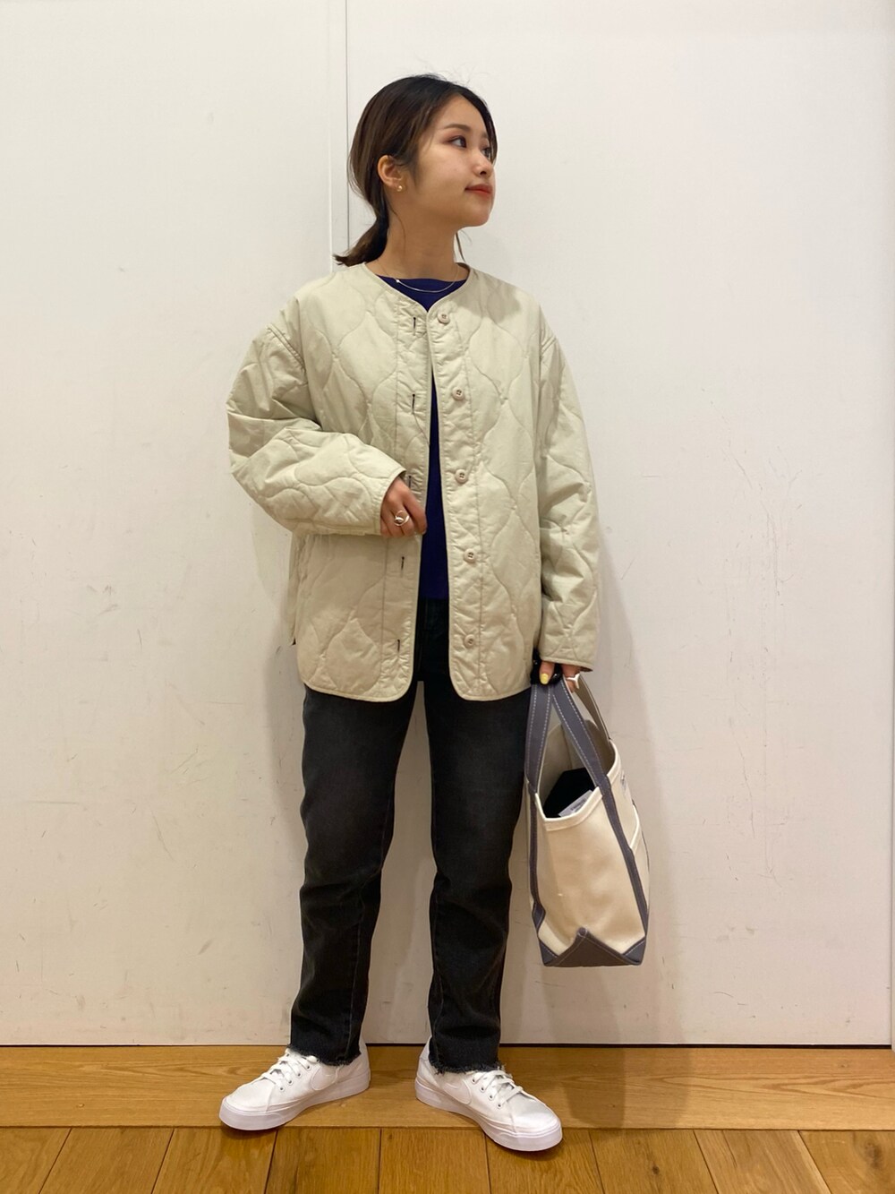 ブラック系のデニムパンツ、ベージュ系のダウンジャケット/コート、ブルー系のTシャツ/カットソーを着用したレディースの春コーディネートの2枚目の写真