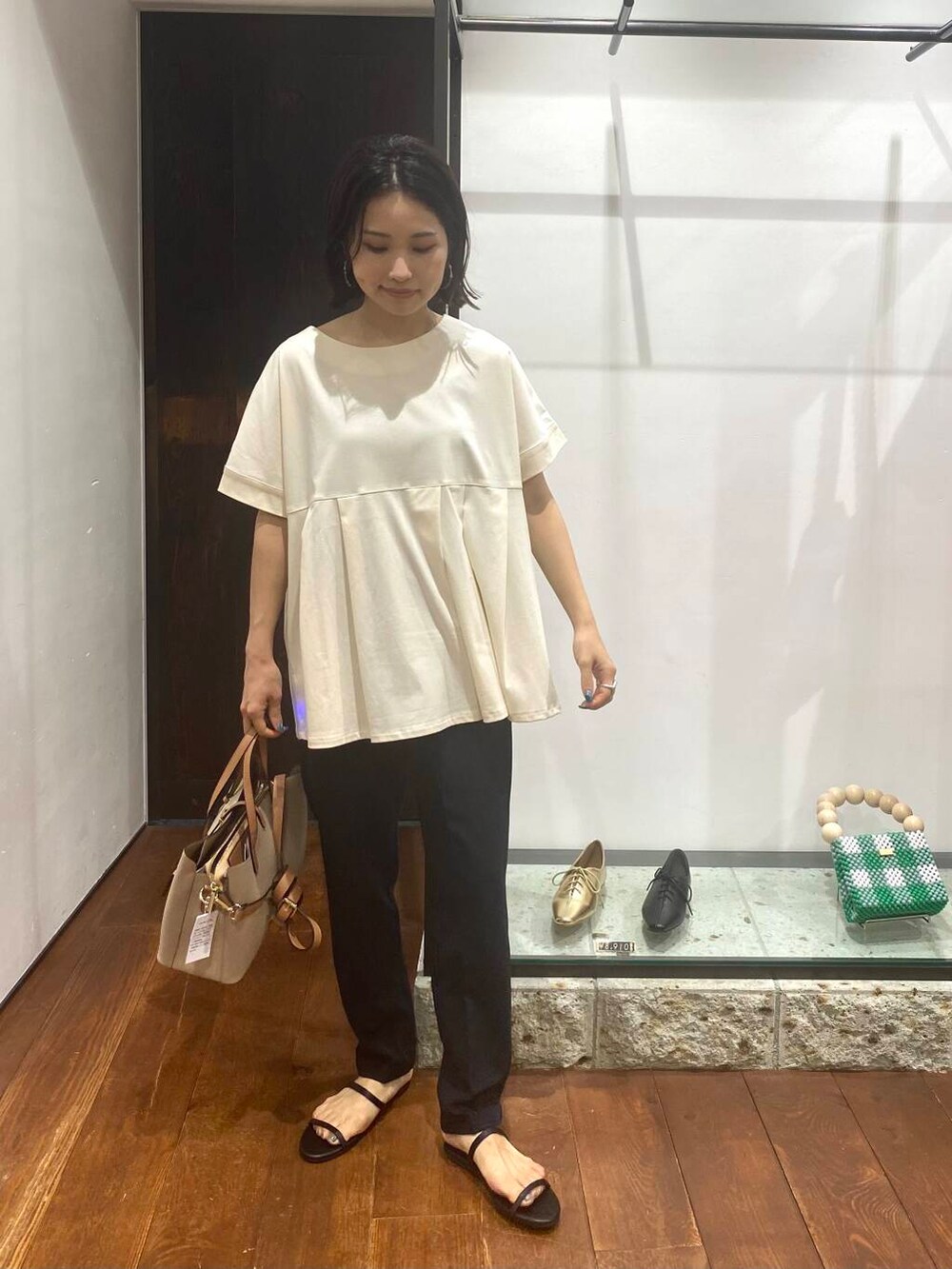 ベージュ系のトートバッグ、ブラック系のサンダル、ホワイト系のTシャツ/カットソーを着用したレディースの夏コーディネートの3枚目の写真